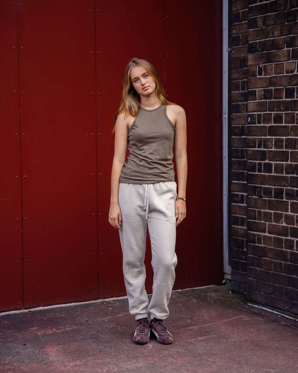 Front-facing view of a woman wearing the American Apparel Racerneck tank top, paired with light blue denim for a clean, minimalist look - heather army