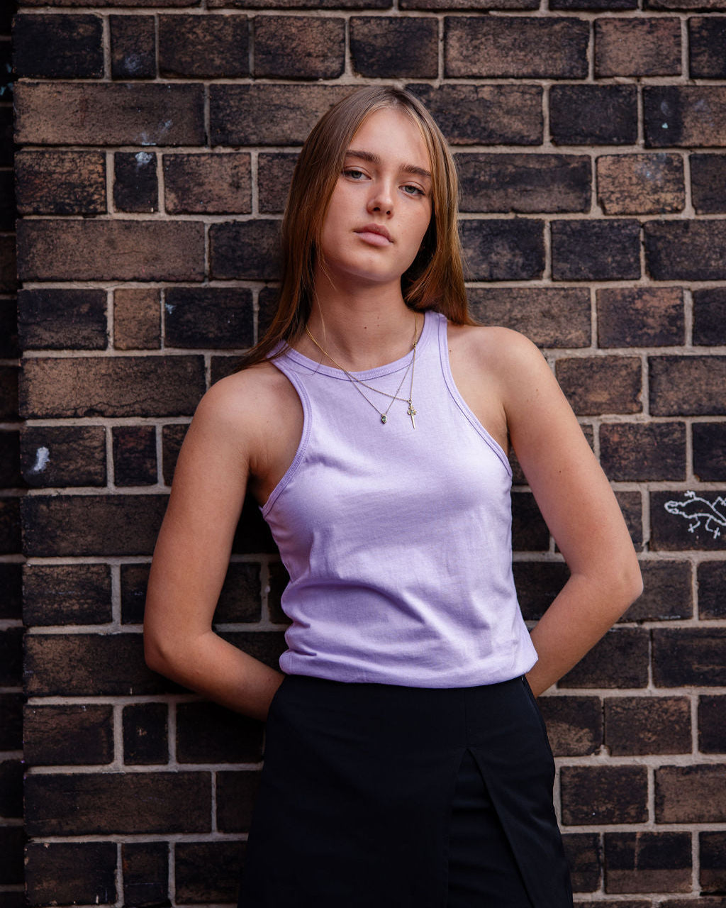 Front-facing view of a woman wearing the American Apparel Racerneck tank top, paired with light blue denim for a clean, minimalist look - lilac