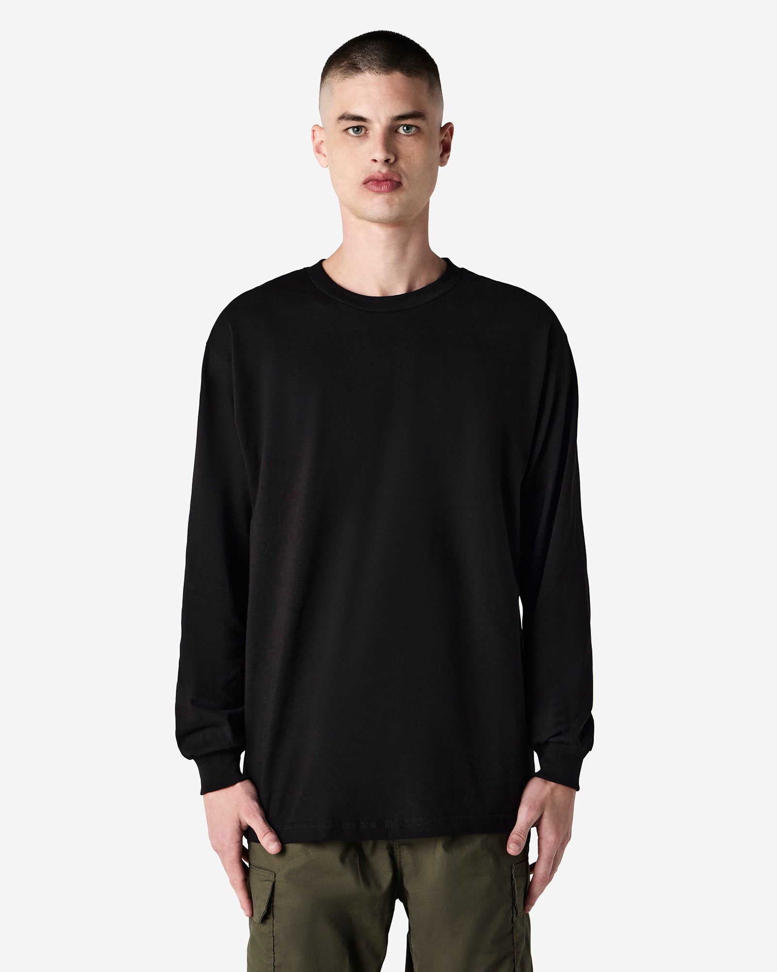 front view of a male Model wearing a black coloured Heavyweight Unisex Long Sleeve Crew Neck Tee, paired with blue jeans, standing against a plain background (front pose) -black