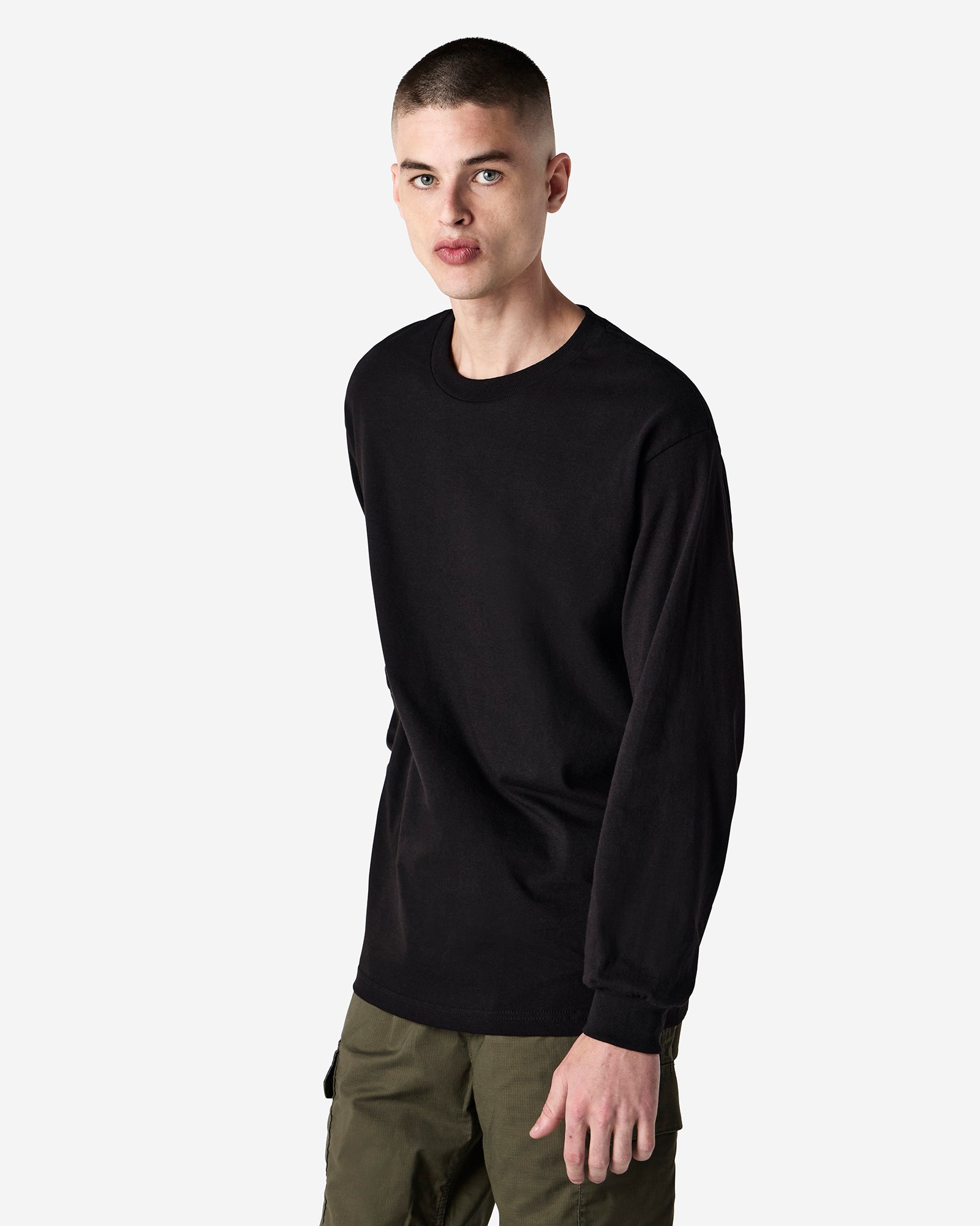 front view of a male Model wearing a black coloured Heavyweight Unisex Long Sleeve Crew Neck Tee, paired with blue jeans, standing against a plain background (front pose) -black
