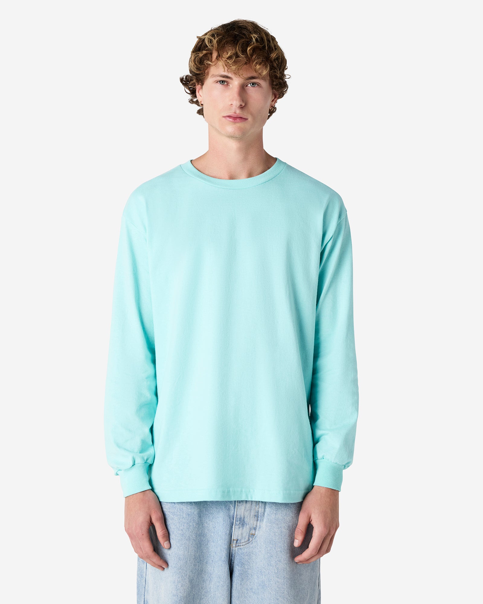front view of a male Model wearing a Celadon colored Heavyweight Unisex Long Sleeve Crew Neck Tee, paired with blue jeans, standing against a plain background (front pose) -celadon