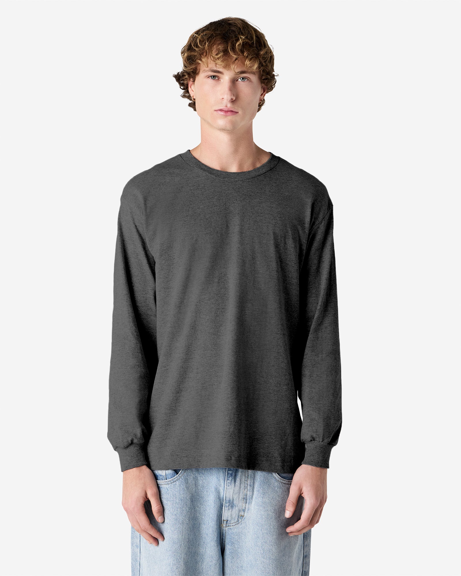 front view of a male Model wearing a Heather Charcoal colored Heavyweight Unisex Long Sleeve Crew Neck Tee, paired with blue jeans, standing against a plain background (front pose) -heather charcoal