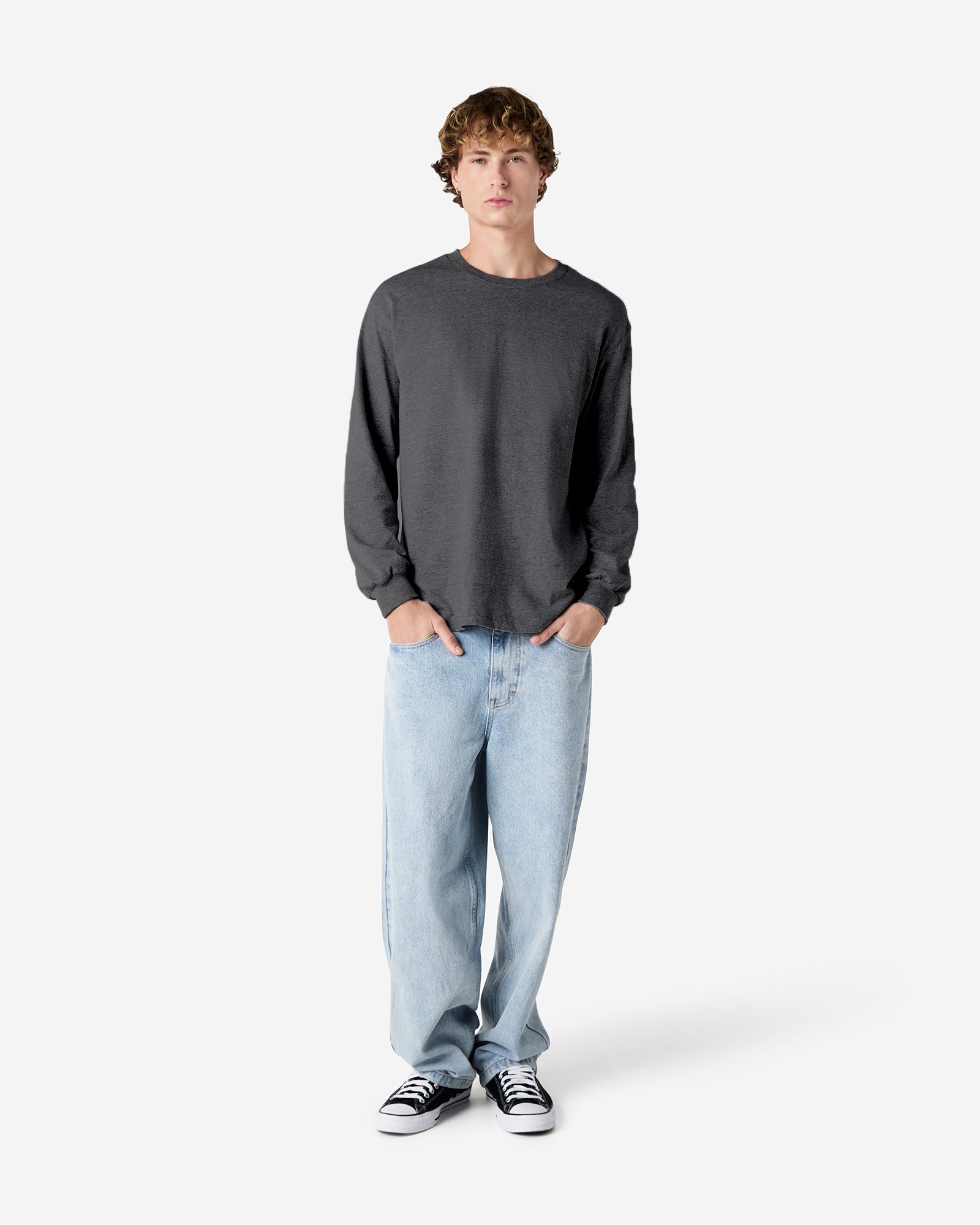 front view of a male Model wearing a Heather Charcoal colored Heavyweight Unisex Long Sleeve Crew Neck Tee, paired with blue jeans, standing against a plain background (front pose) -heather charcoal