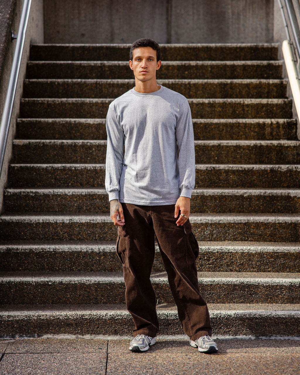 front view of a male Model wearing a Heather Charcoal Grey Heavyweight Unisex Long Sleeve Crew Neck Tee, paired with blue jeans, standing against a plain background (front pose) -heather Grey