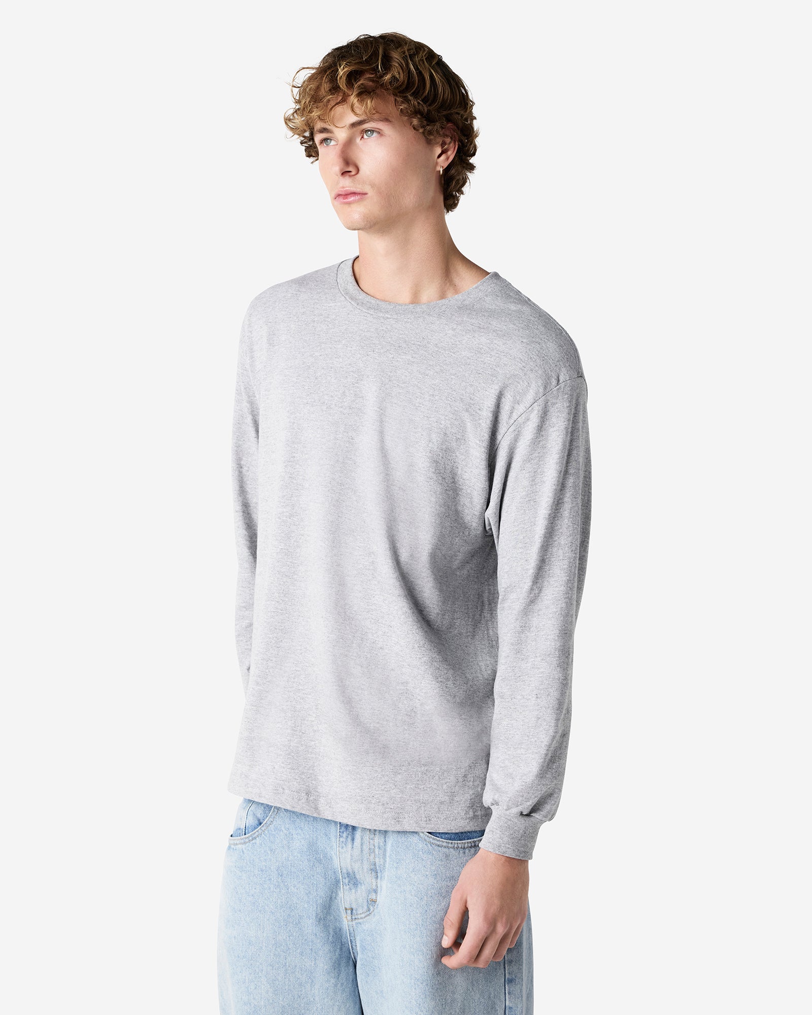 front view of a male Model wearing a Heather Charcoal Grey Heavyweight Unisex Long Sleeve Crew Neck Tee, paired with blue jeans, standing against a plain background (front pose) -heather Grey