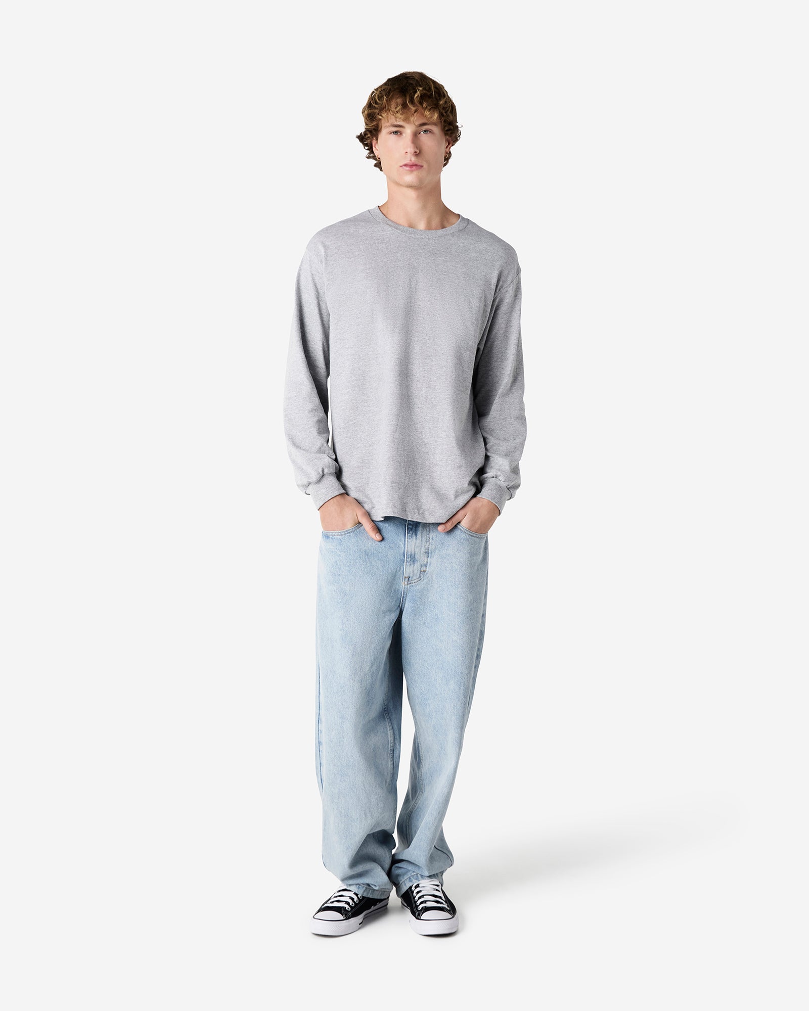 front view of a male Model wearing a Heather Charcoal Grey Heavyweight Unisex Long Sleeve Crew Neck Tee, paired with blue jeans, standing against a plain background (front pose) -heather Grey