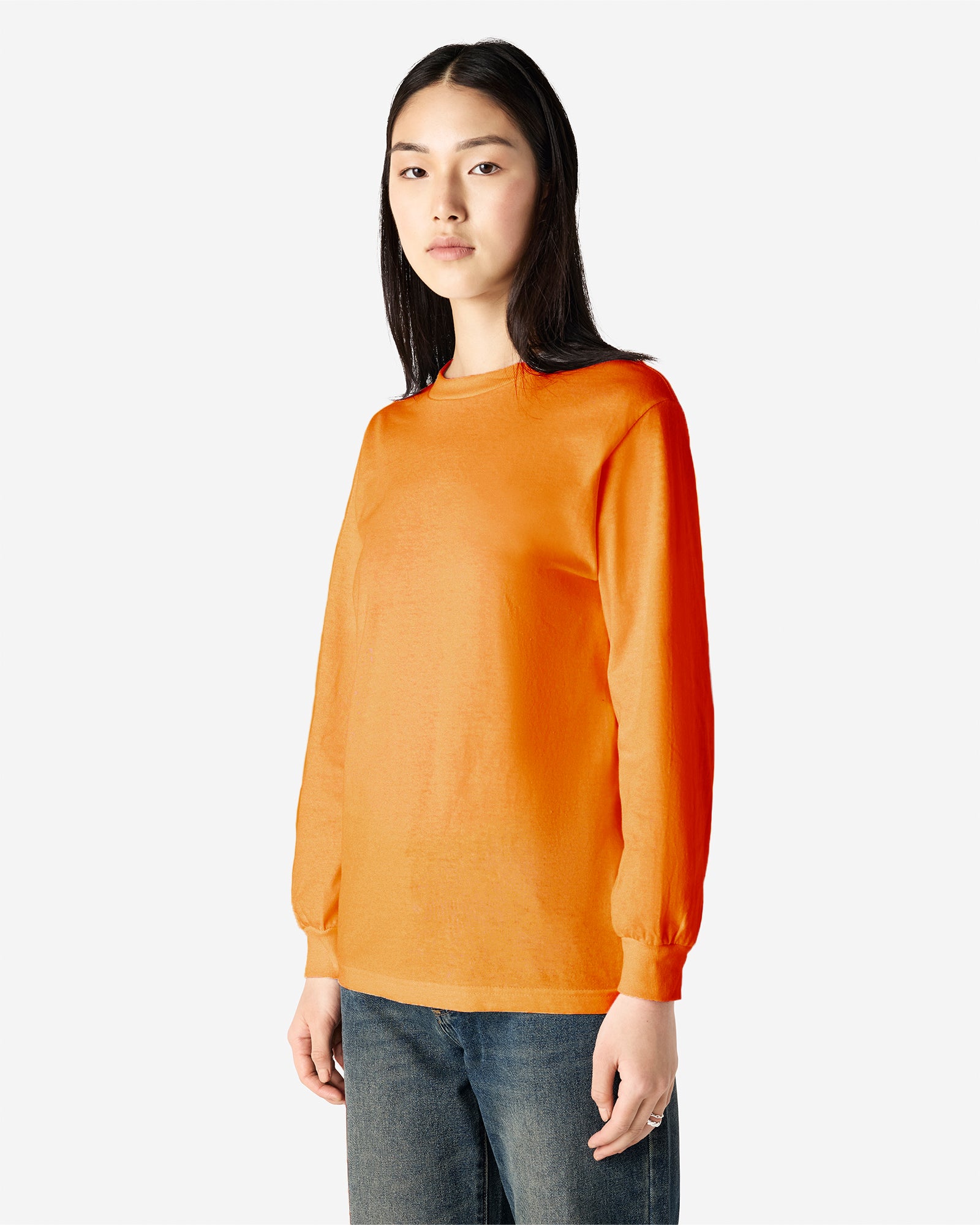 front view of a female Model wearing a Heather Orange Heavyweight Unisex Long Sleeve Crew Neck Tee, paired with blue jeans, standing against a plain background (front pose) -orange