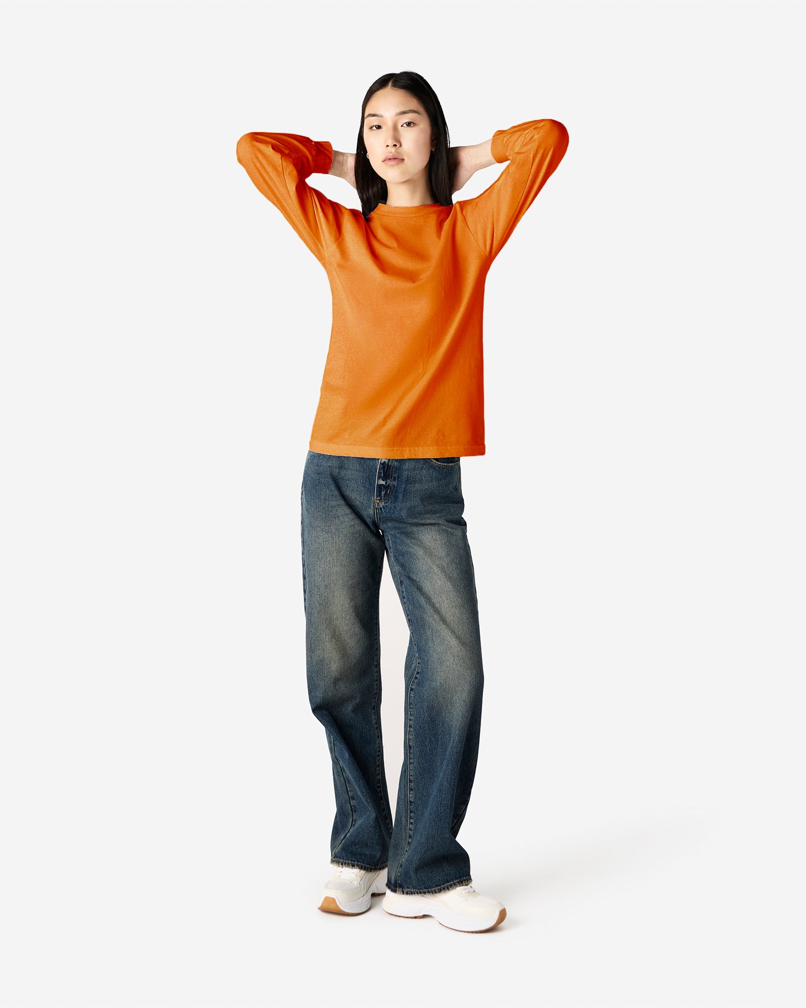 front view of a female Model wearing a Heather Orange Heavyweight Unisex Long Sleeve Crew Neck Tee, paired with blue jeans, standing against a plain background (front pose) -orange