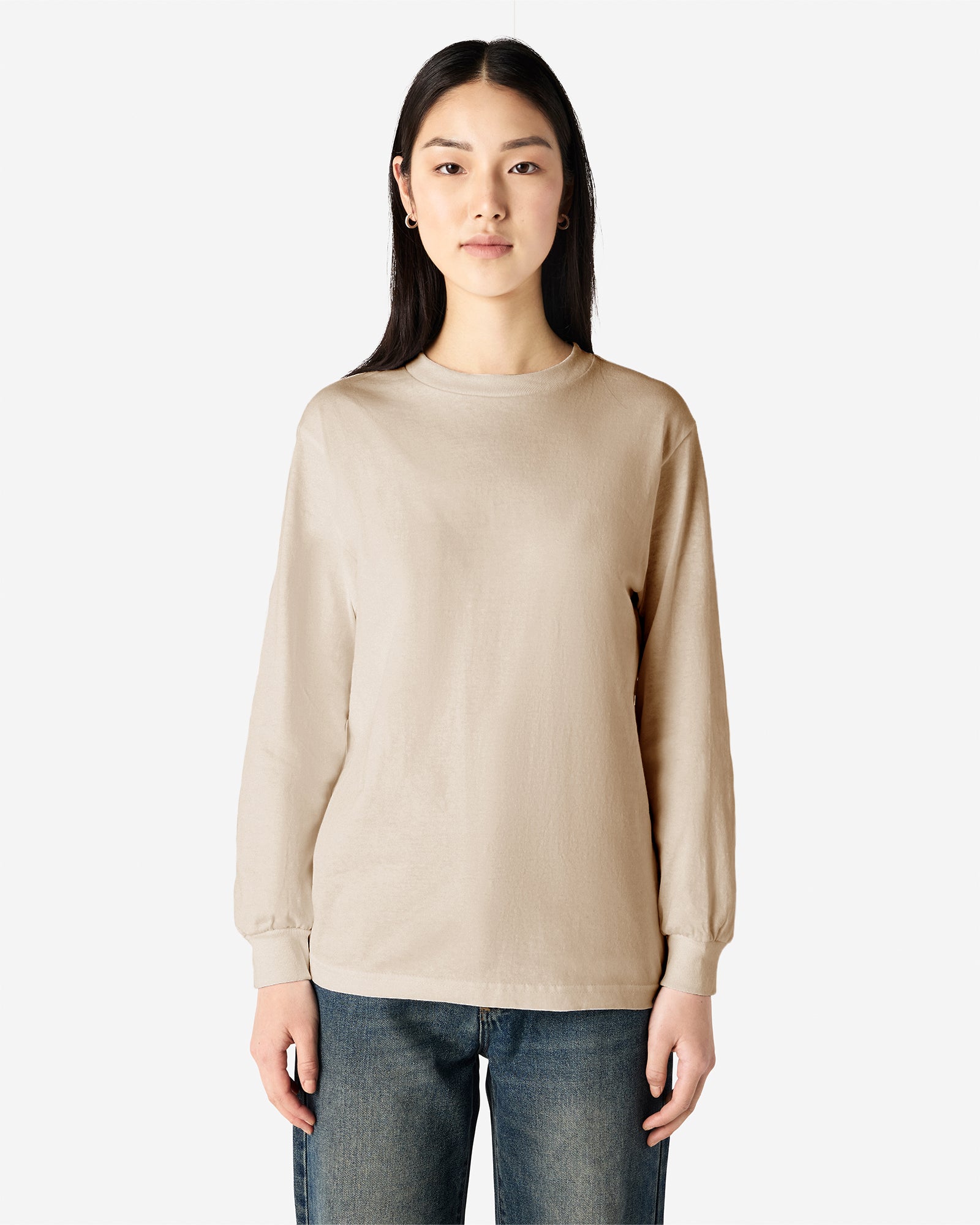 front view of a female Model wearing a Sand colored Heavyweight Unisex Long Sleeve Crew Neck Tee, paired with blue jeans, standing against a plain background (front pose) -sand