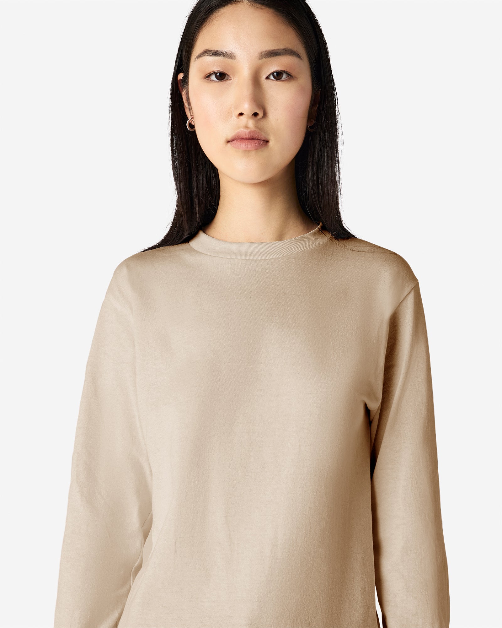 front view of a female Model wearing a Sand colored Heavyweight Unisex Long Sleeve Crew Neck Tee, paired with blue jeans, standing against a plain background (front pose) -sand