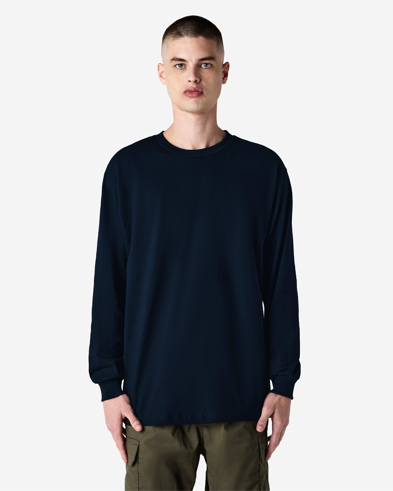 front view of a male Model wearing a True Navy colored Heavyweight Unisex Long Sleeve Crew Neck Tee, paired with blue jeans, standing against a plain background (front pose) -true navy