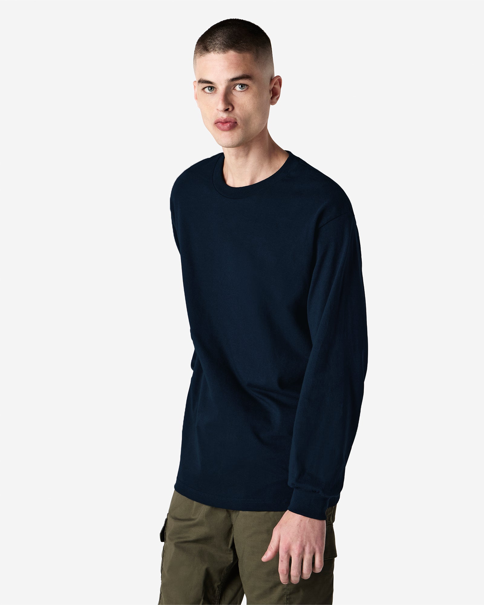 front view of a male Model wearing a True Navy colored Heavyweight Unisex Long Sleeve Crew Neck Tee, paired with blue jeans, standing against a plain background (front pose) -true navy