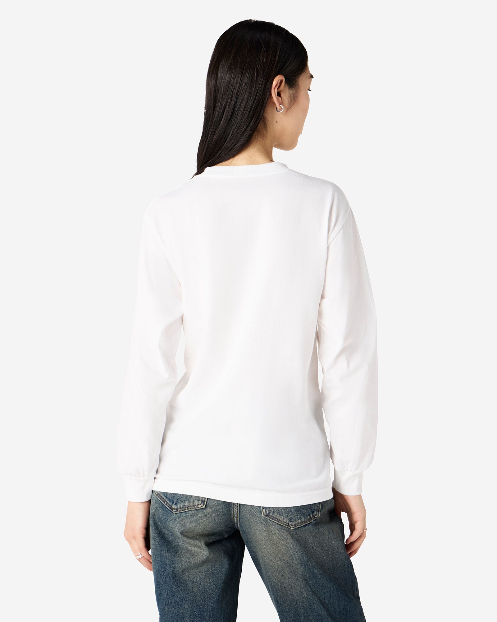 front view of a female Model wearing a White colored Heavyweight Unisex Long Sleeve Crew Neck Tee, paired with blue jeans, standing against a plain background (front pose) -white