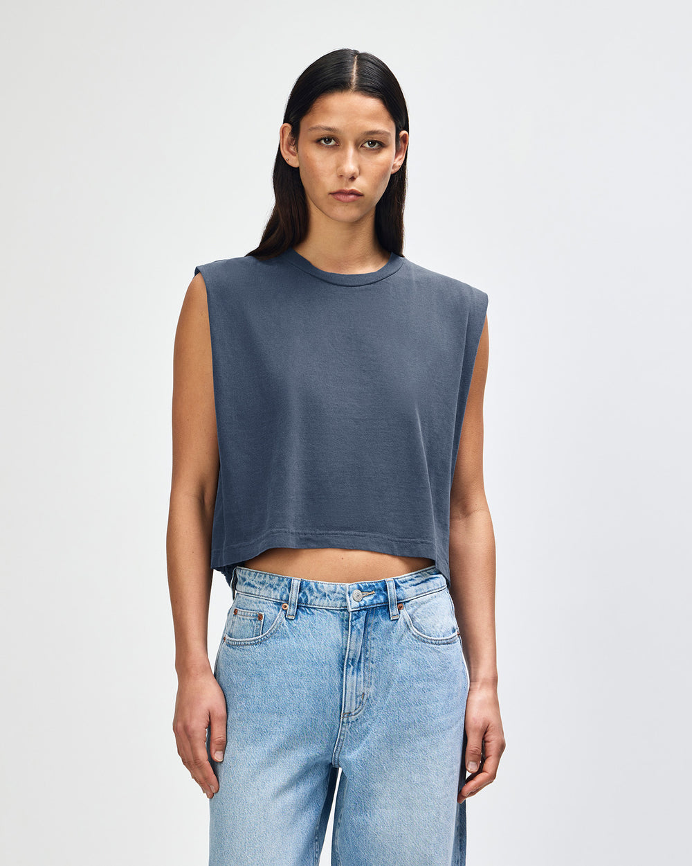 next image of Women's Muscle T-Shirt: Model wearing a faded navy Garment Dyed Women's Muscle Tee, sleeveless, paired with light blue jeans, standing against a plain white background (front pose) -navy