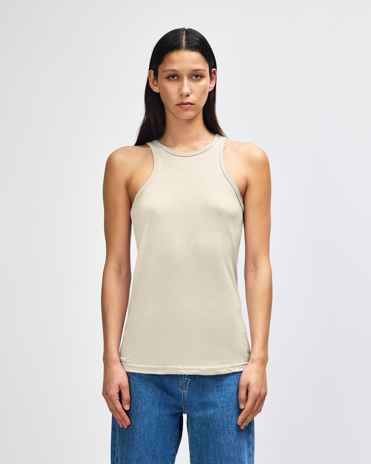 Front-facing view of a woman wearing the American Apparel Racerneck tank top, paired with light blue denim for a clean, minimalist look - heather bone