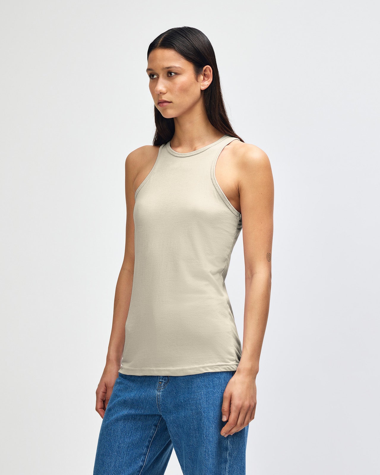 Front-facing view of a woman wearing the American Apparel Racerneck tank top, paired with light blue denim for a clean, minimalist look - heather bone