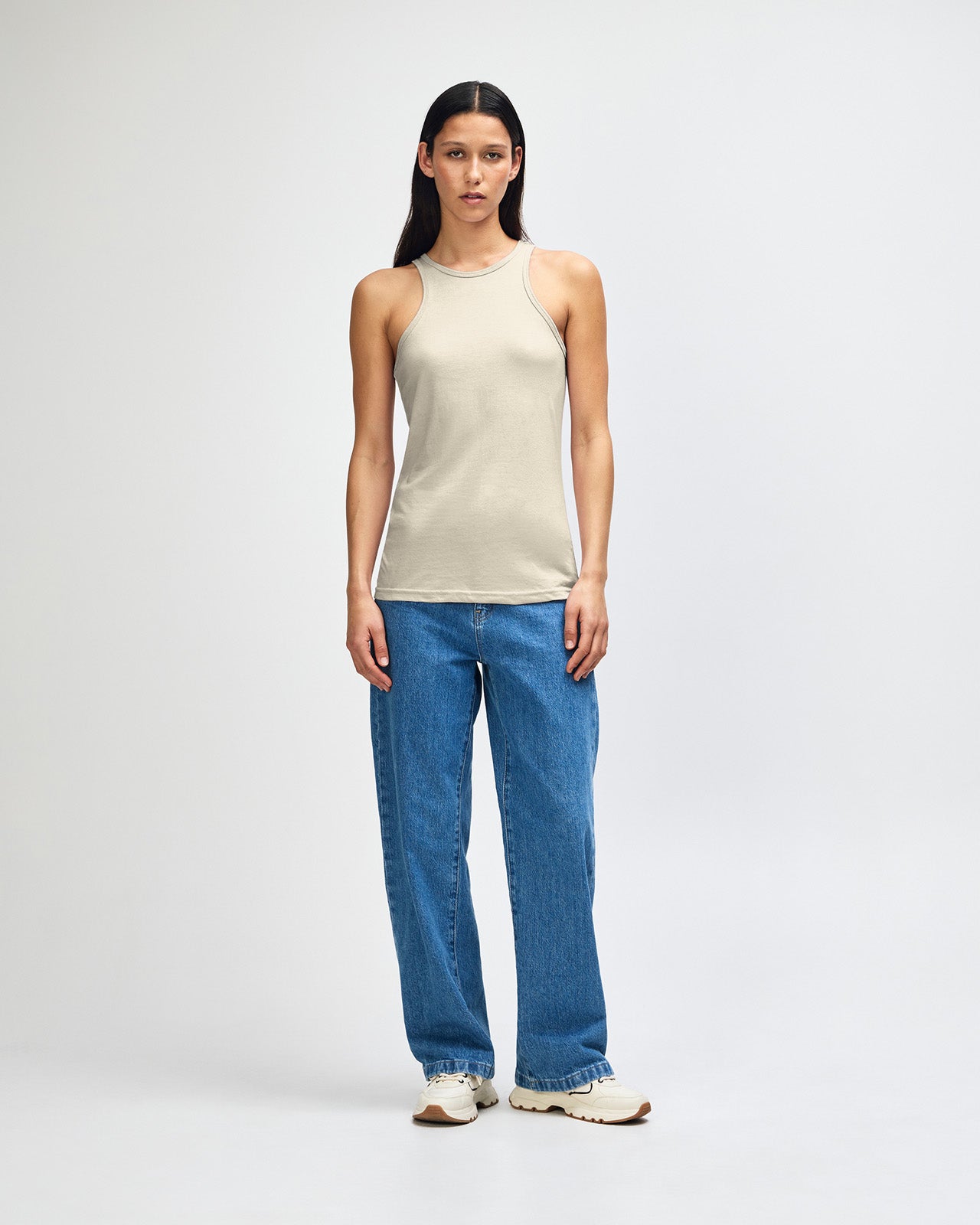 Front-facing view of a woman wearing the American Apparel Racerneck tank top, paired with light blue denim for a clean, minimalist look - heather bone