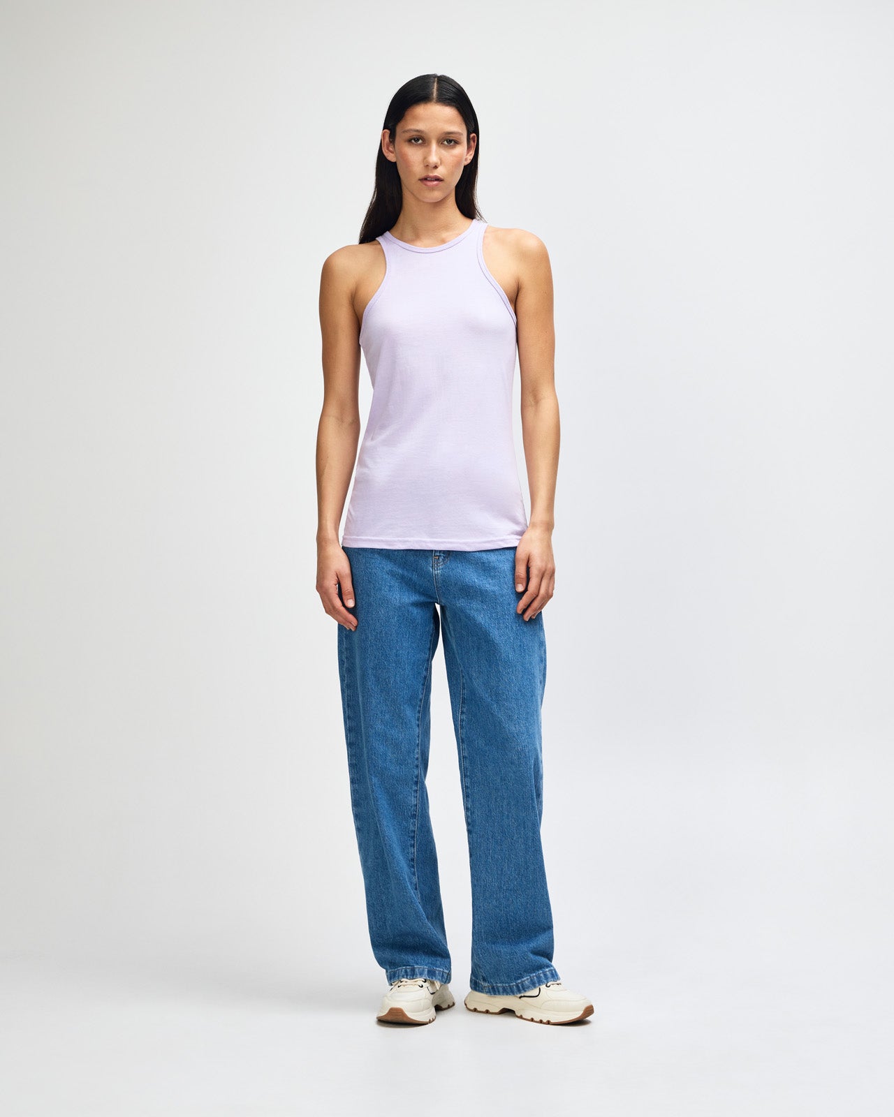 Front-facing view of a woman wearing the American Apparel Racerneck tank top, paired with light blue denim for a clean, minimalist look - lilac