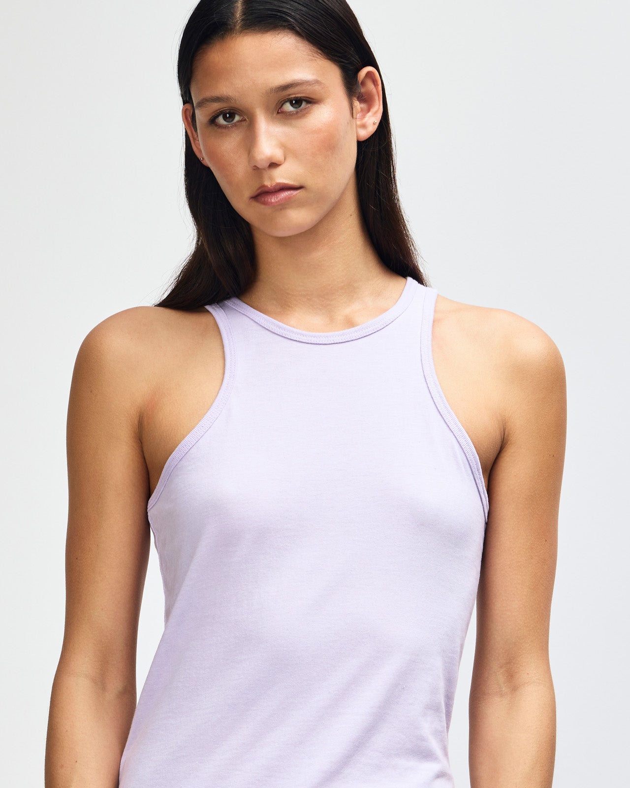 Front-facing view of a woman wearing the American Apparel Racerneck tank top, paired with light blue denim for a clean, minimalist look - lilac