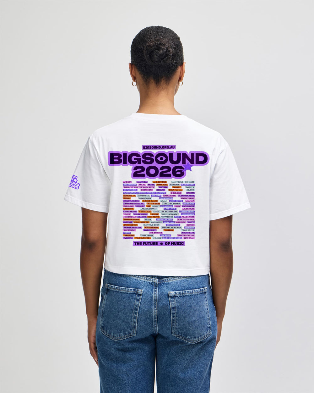 next image of BIGSOUND Lineup Cropped T-shirt : A person shown from the back wearing a white graphic T shirt and blue jeans against a light gray studio background. The shirt features a large purple and multicolor 'BIGSOUND 2026' graphic with text reading 'MEXICAN SOUND' and 'THE FUTURE IS IN YOUR HAND' -white