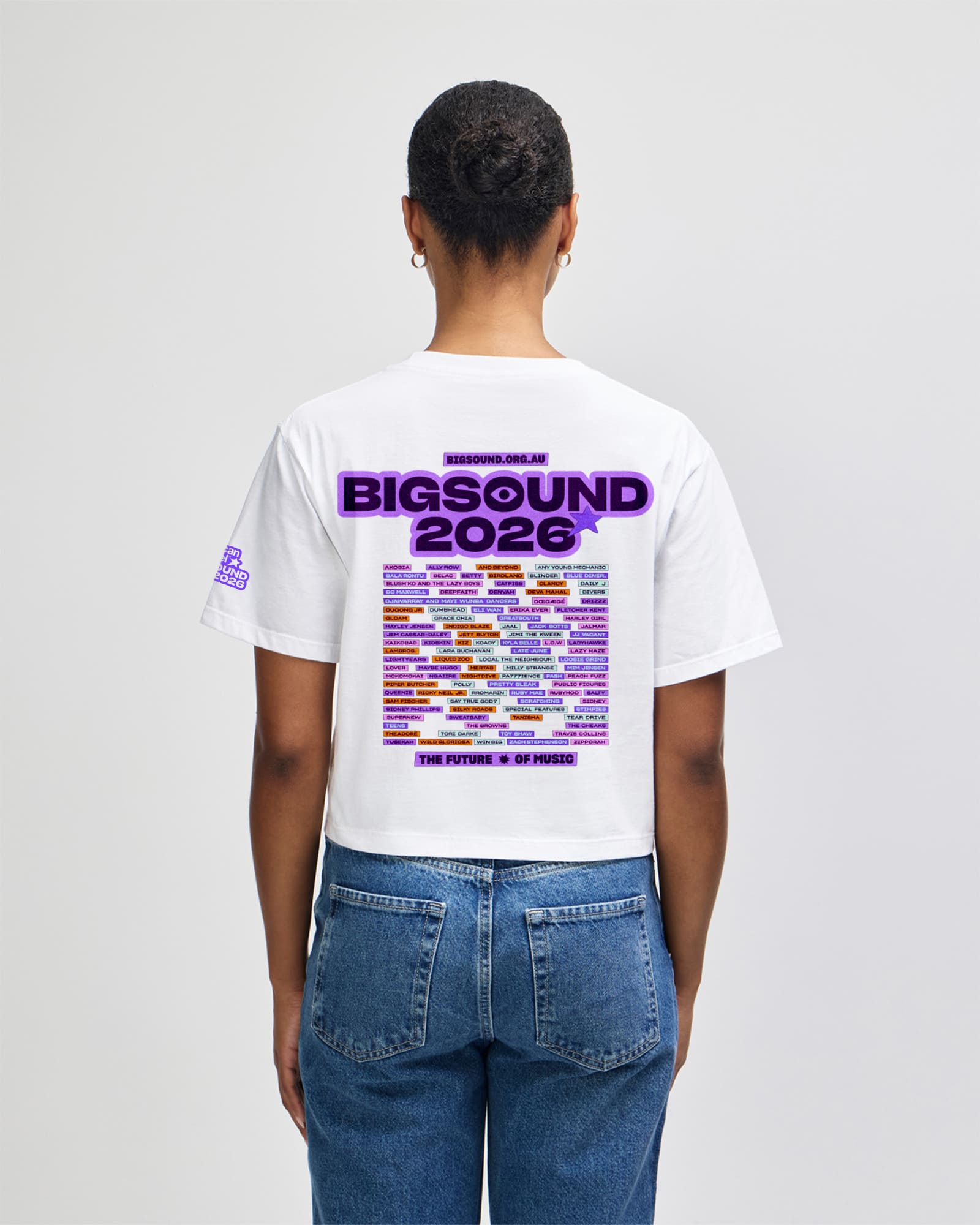 A person shown from the back wearing a white graphic T shirt and blue jeans against a light gray studio background. The shirt features a large purple and multicolor 'BIGSOUND 2026' graphic with text reading 'MEXICAN SOUND' and 'THE FUTURE IS IN YOUR HAND' -white