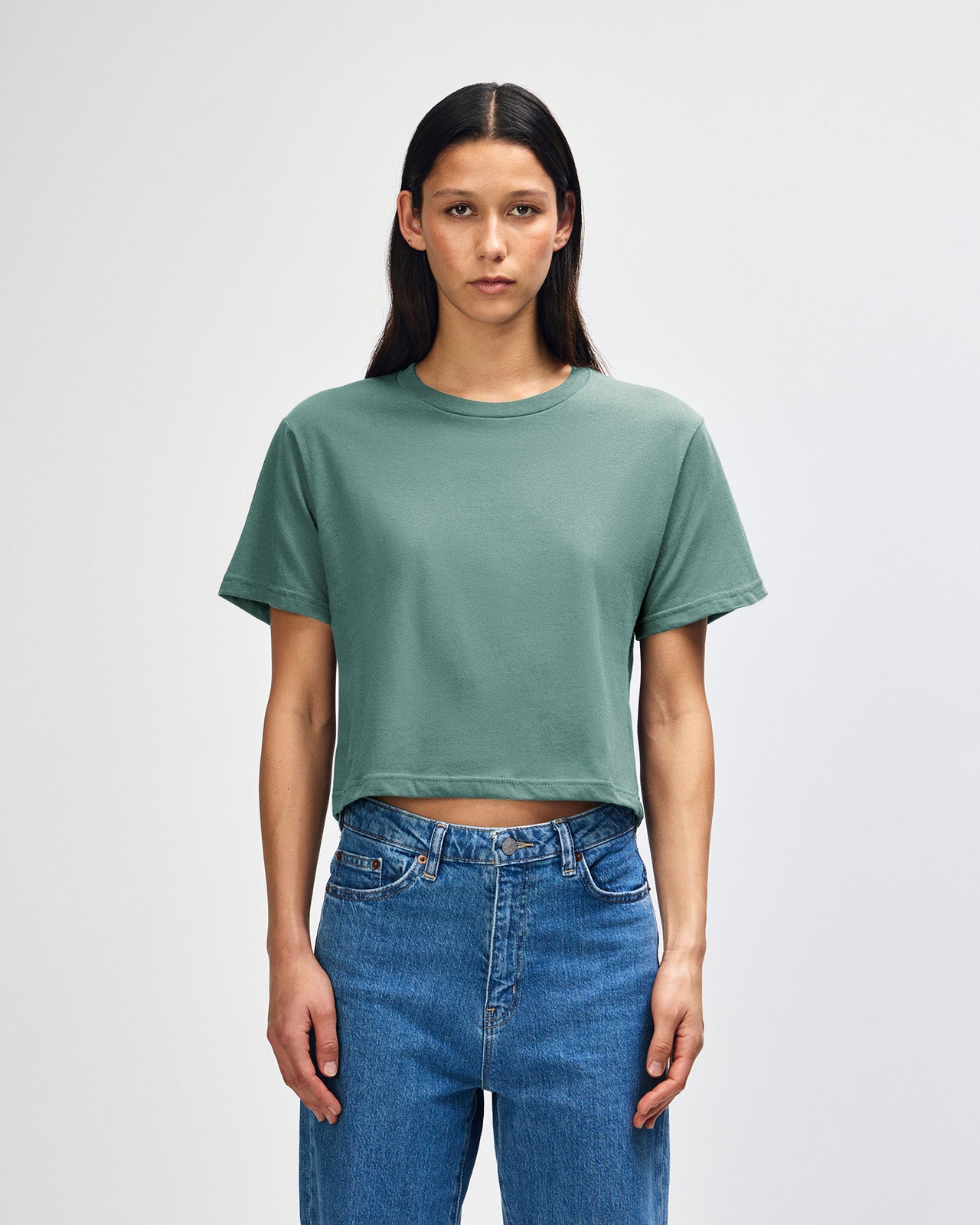 Female model wearing an American Apparel Fine Jersey Women's Boxy Tee in arctic, paired with blue jeans, standing against a plain background (front pose) -arctic