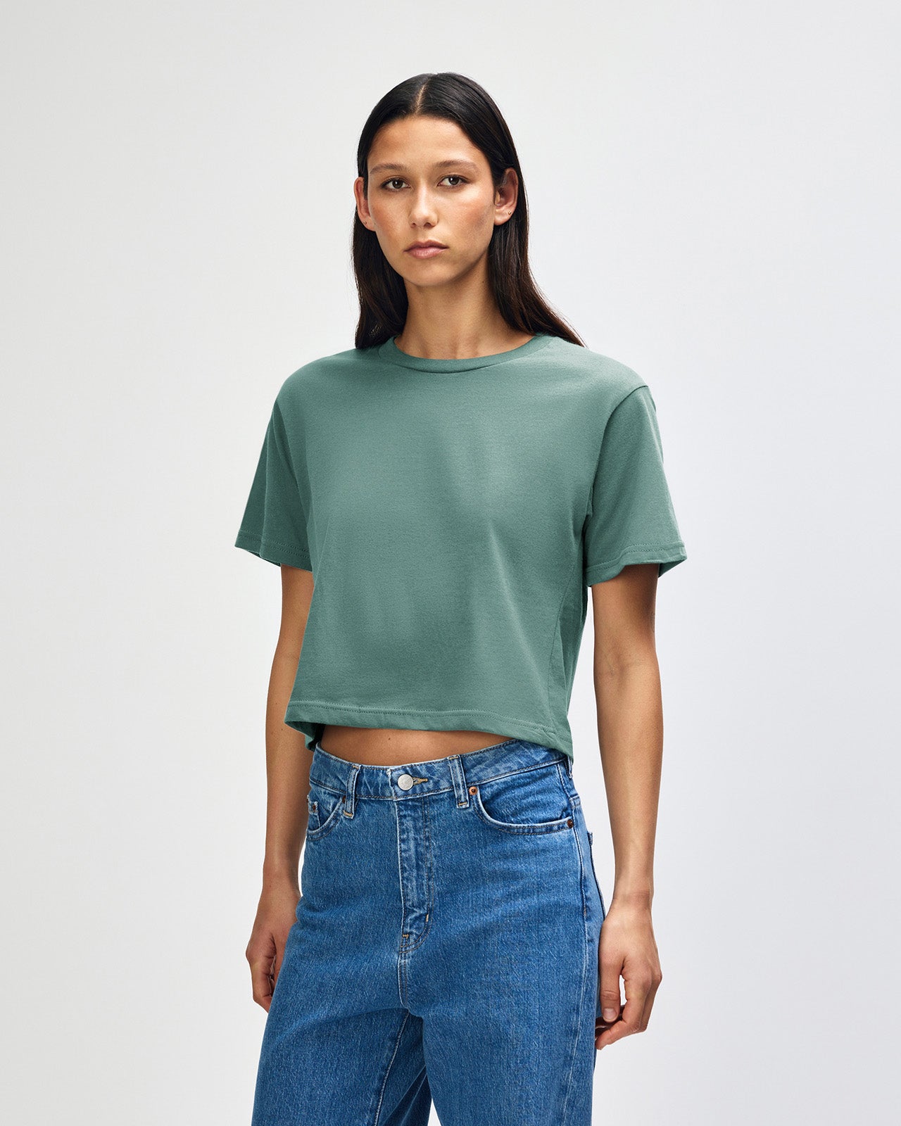 Female model wearing an American Apparel Fine Jersey Women's Boxy Tee in arctic, paired with blue jeans, standing against a plain background (front pose) -arctic