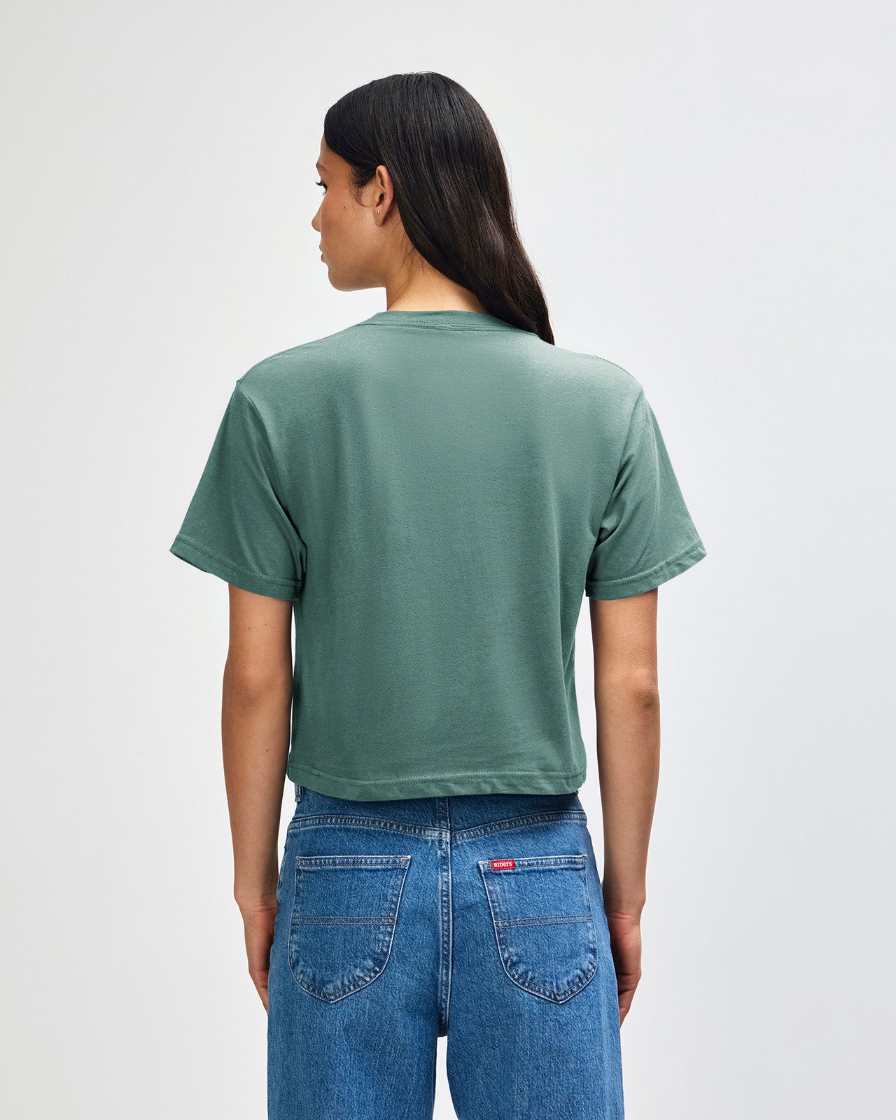 Female model wearing an American Apparel Fine Jersey Women's Boxy Tee in arctic, paired with blue jeans, standing against a plain background (front pose) -arctic