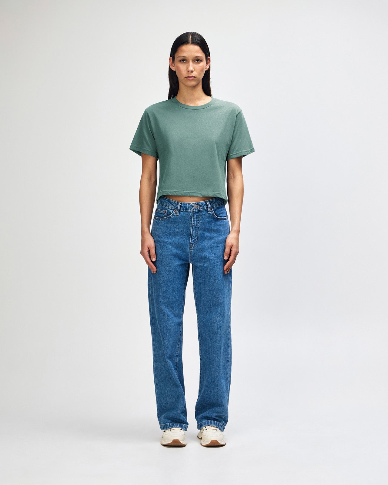 Female model wearing an American Apparel Fine Jersey Women's Boxy Tee in arctic, paired with blue jeans, standing against a plain background (front pose) -arctic