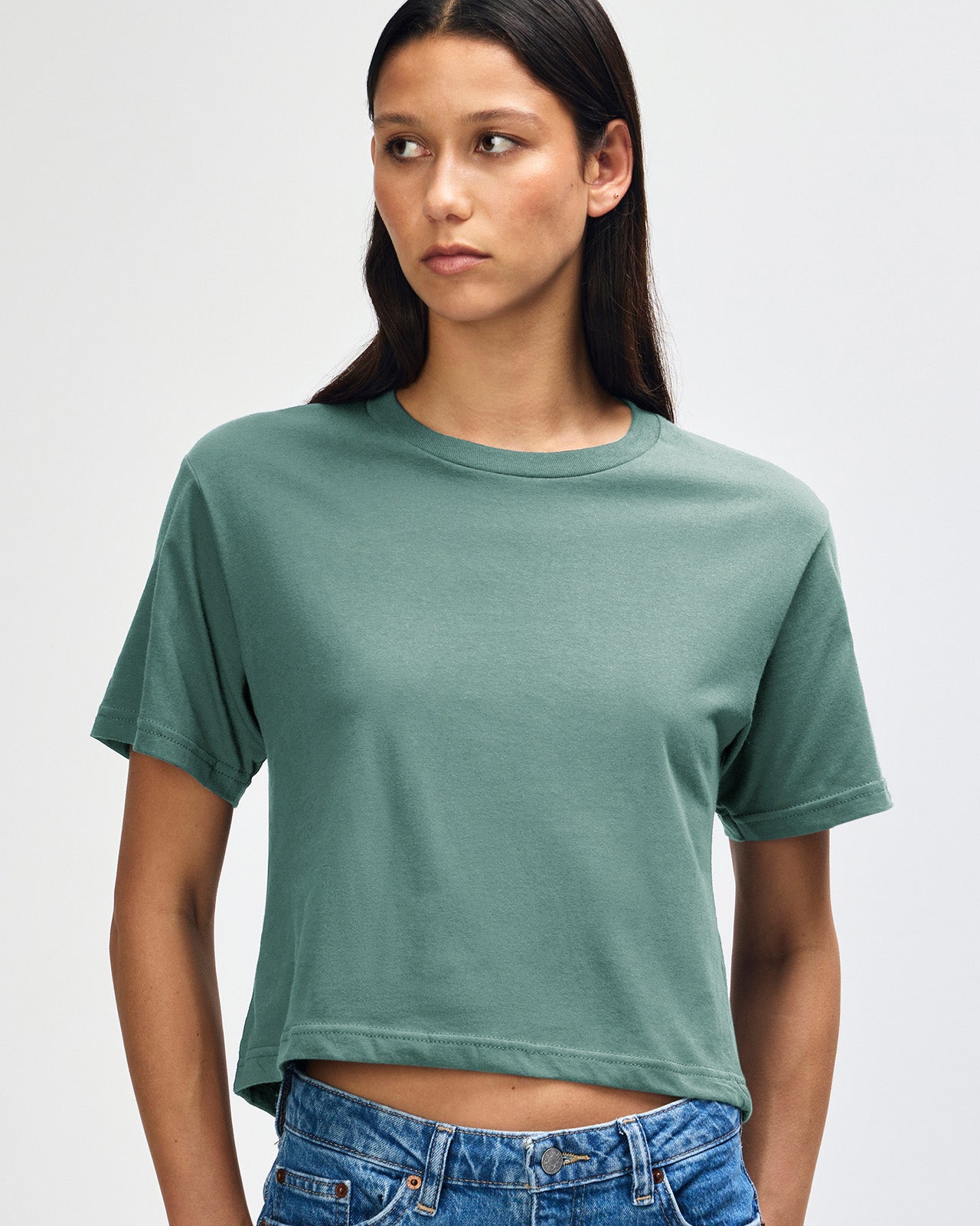 Female model wearing an American Apparel Fine Jersey Women's Boxy Tee in arctic, paired with blue jeans, standing against a plain background (front pose) -arctic