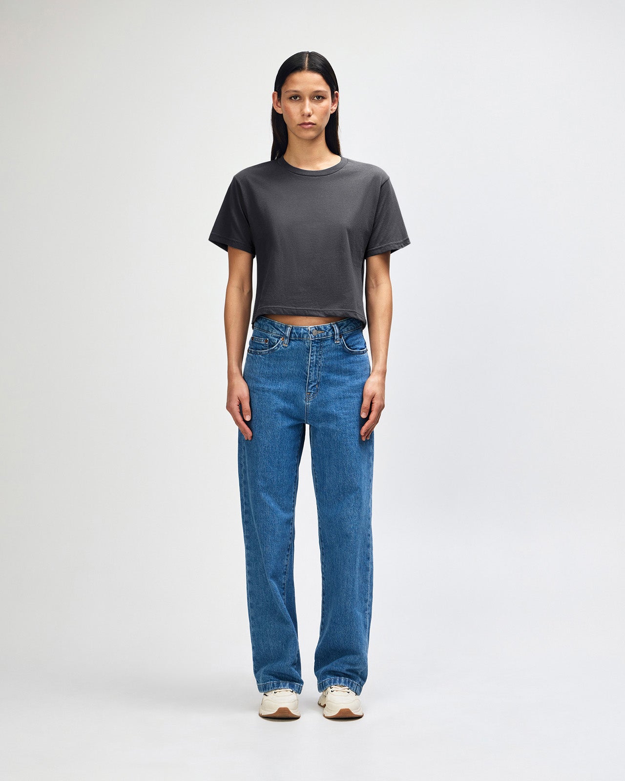 Female model wearing an American Apparel Fine Jersey Women's Boxy Tee in arctic, paired with blue jeans, standing against a plain background (front pose) -asphalt