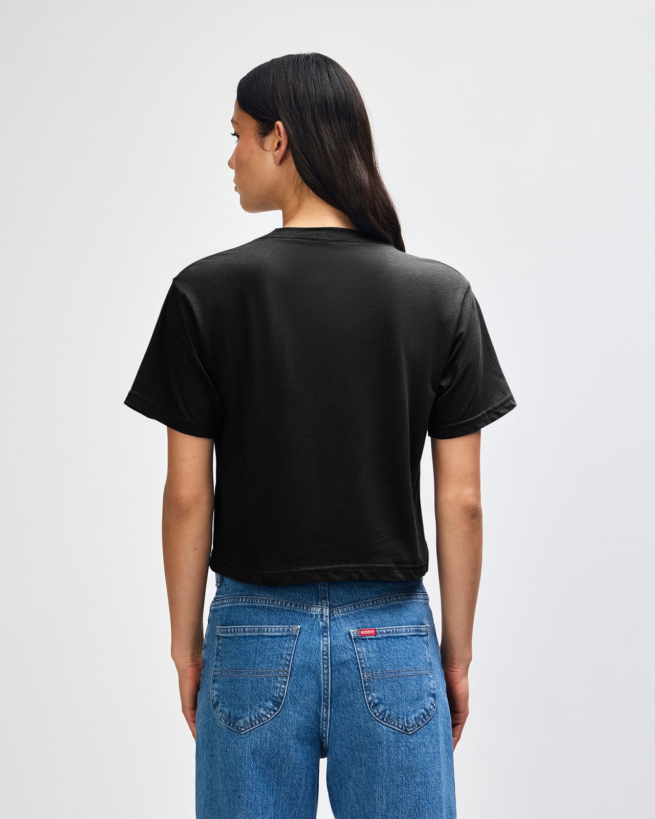 Female model wearing an American Apparel Fine Jersey Women's Boxy Tee in Black, paired with blue jeans, standing against a plain background (front pose) -black