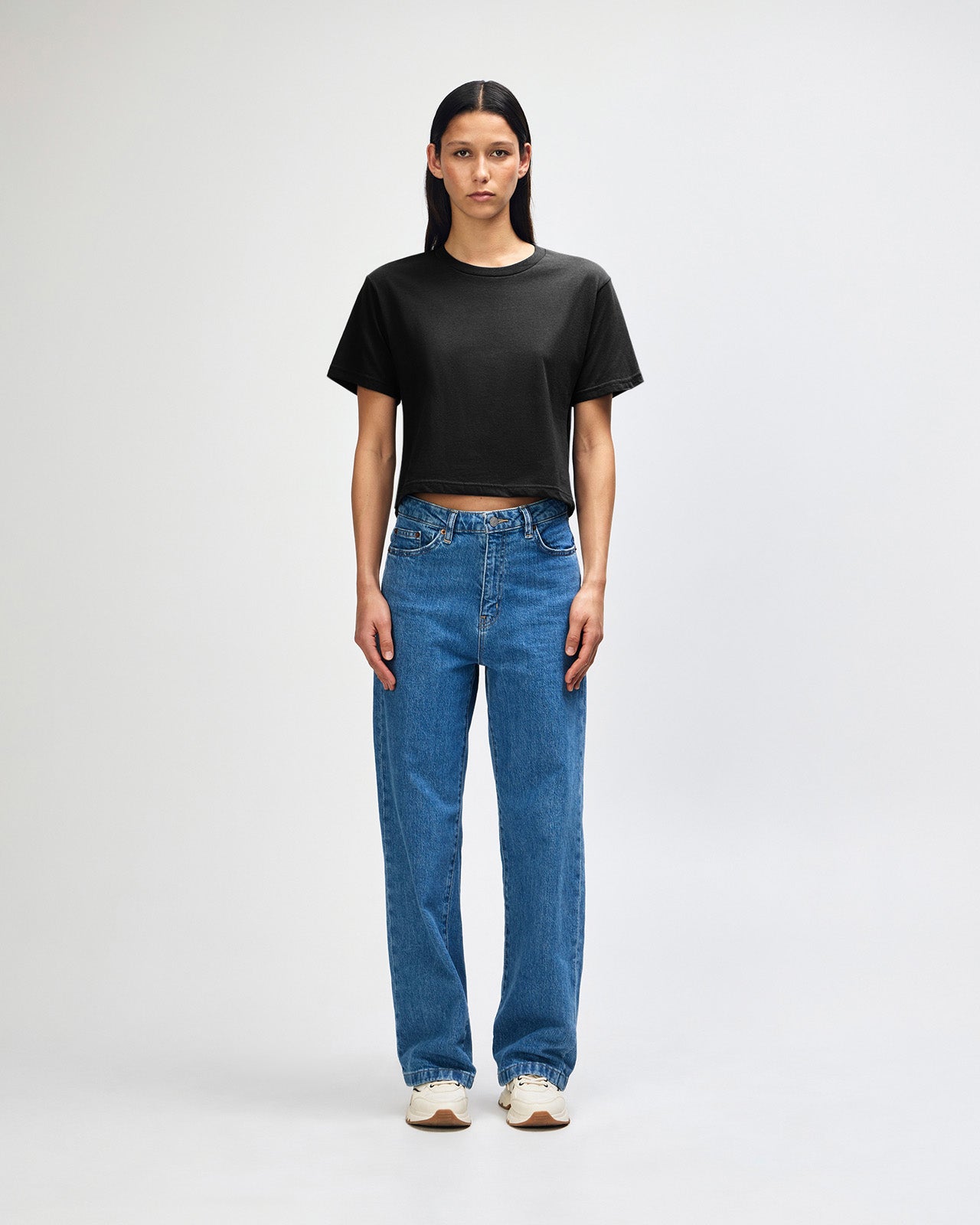 Female model wearing an American Apparel Fine Jersey Women's Boxy Tee in Black, paired with blue jeans, standing against a plain background (front pose) -black