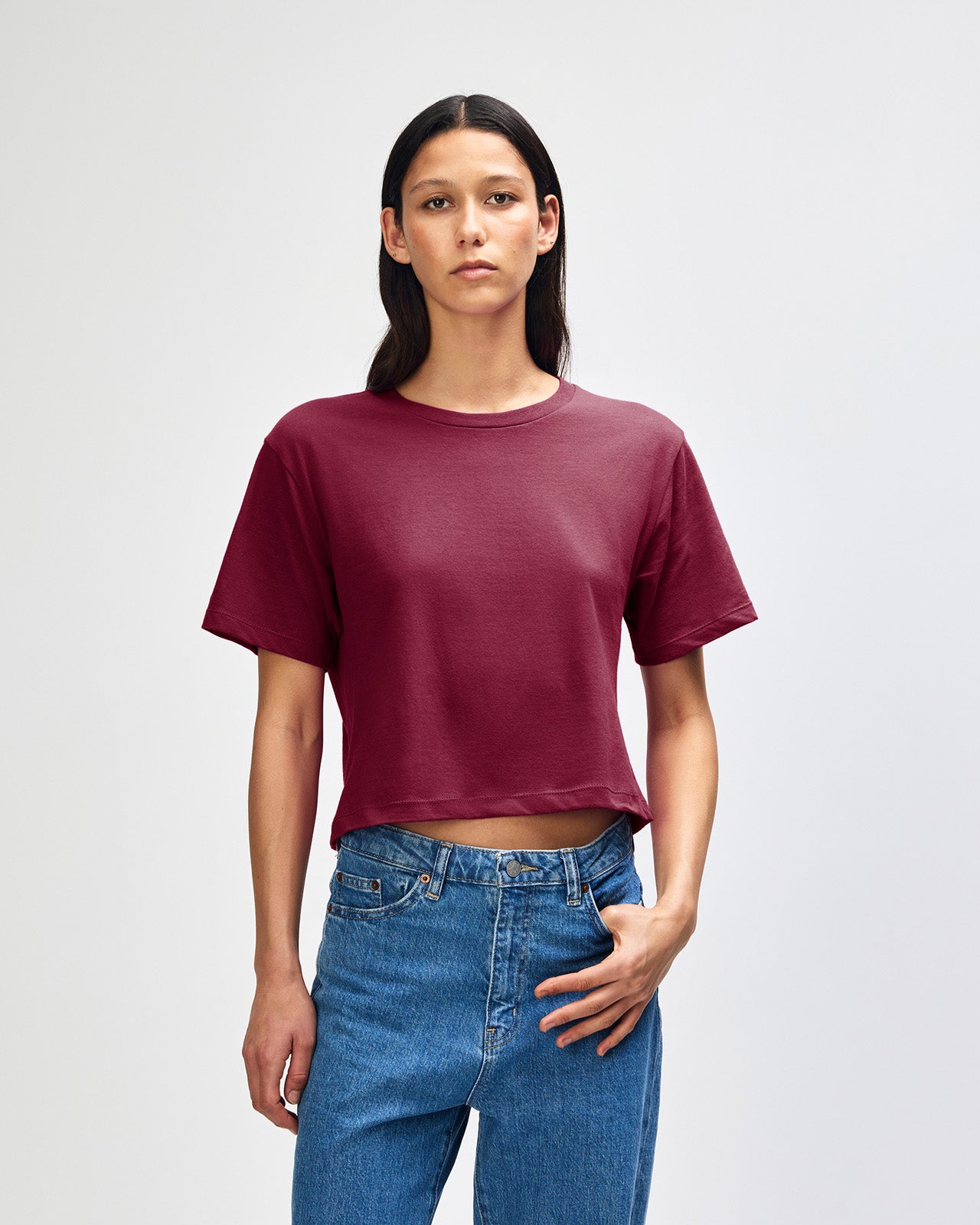 Female model wearing an American Apparel Fine Jersey Women's Boxy Tee in Burgundy, paired with blue jeans, standing against a plain background (front pose) -burgundy