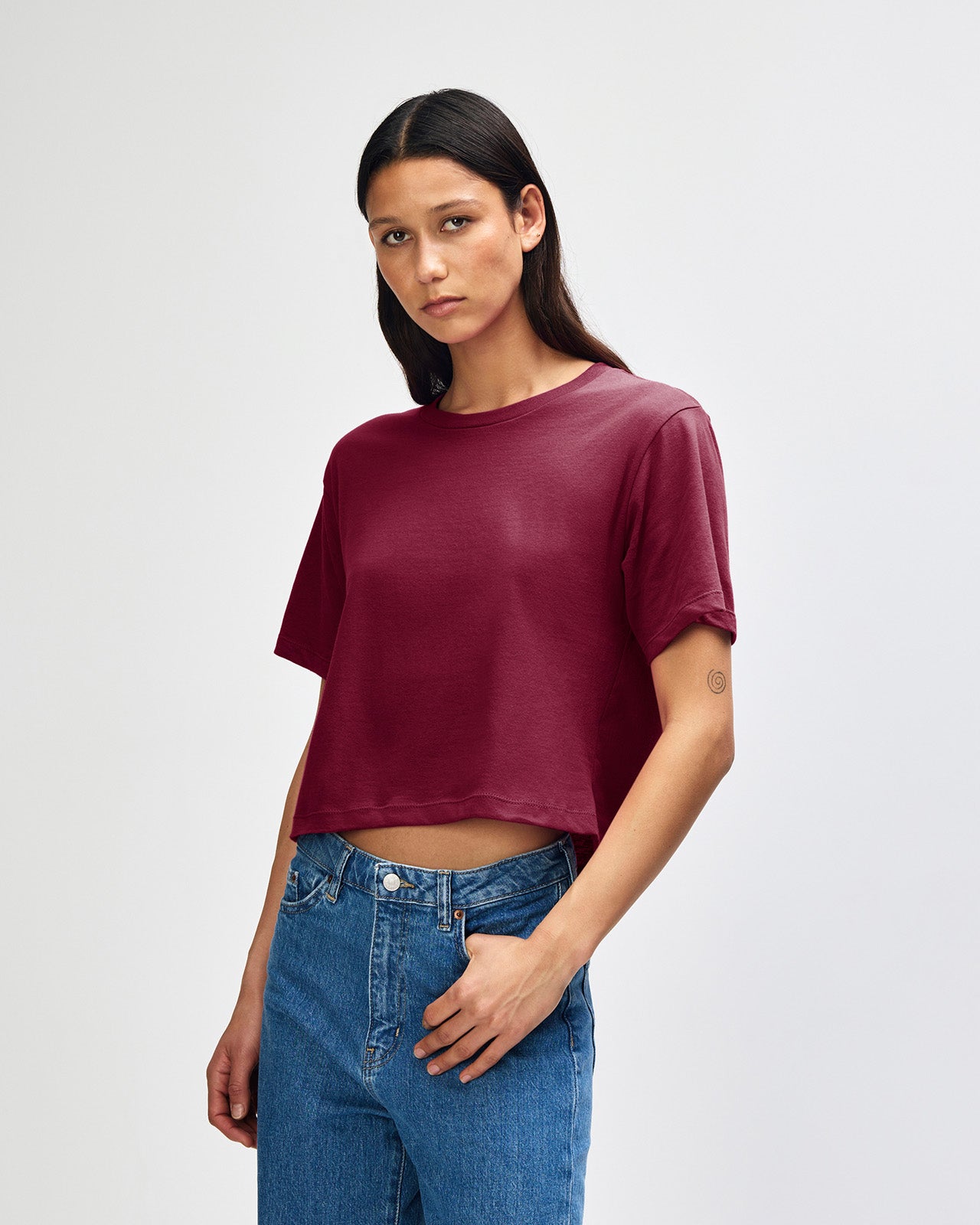 Female model wearing an American Apparel Fine Jersey Women's Boxy Tee in Burgundy, paired with blue jeans, standing against a plain background (front pose) -burgundy