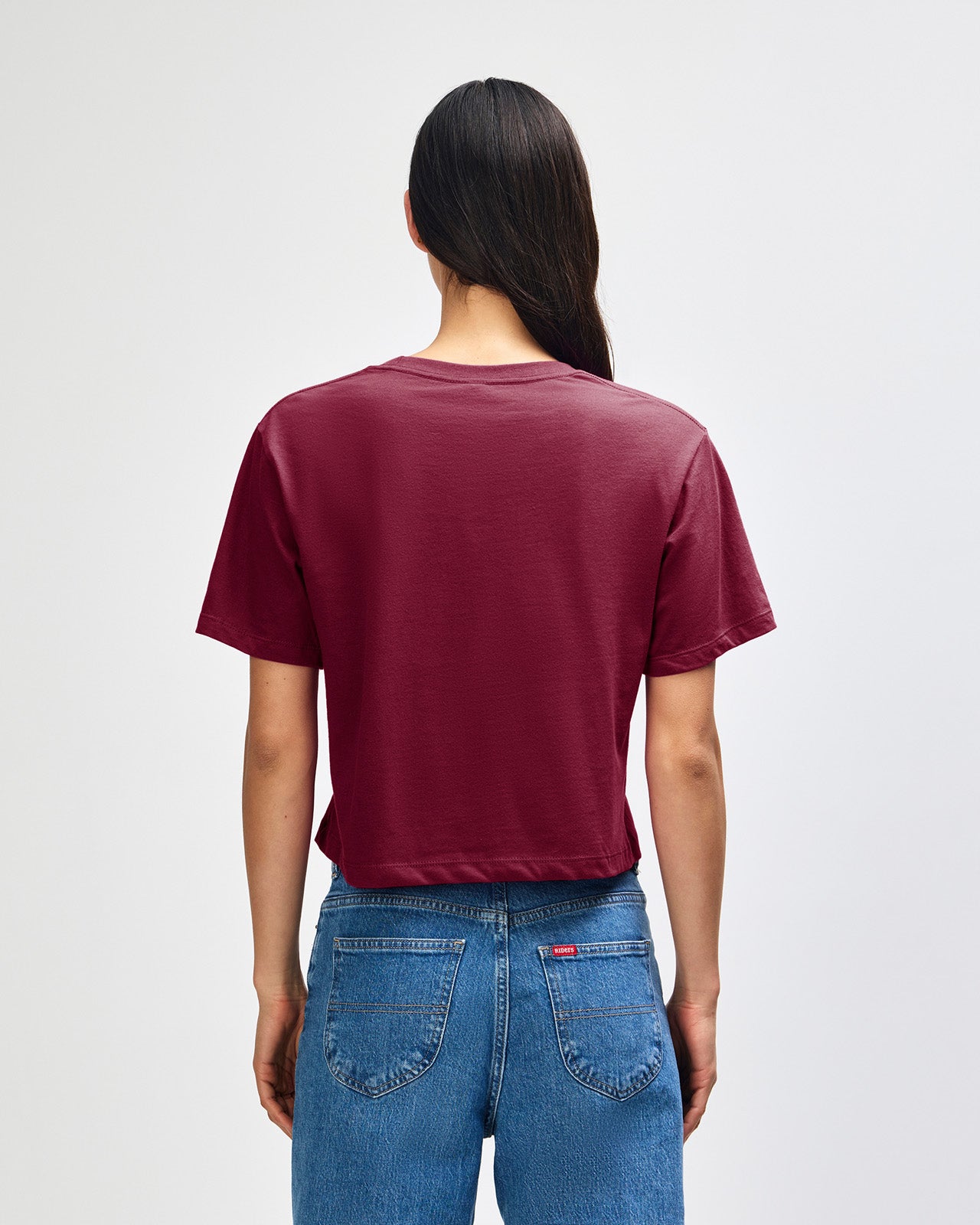 Female model wearing an American Apparel Fine Jersey Women's Boxy Tee in Burgundy, paired with blue jeans, standing against a plain background (front pose) -burgundy