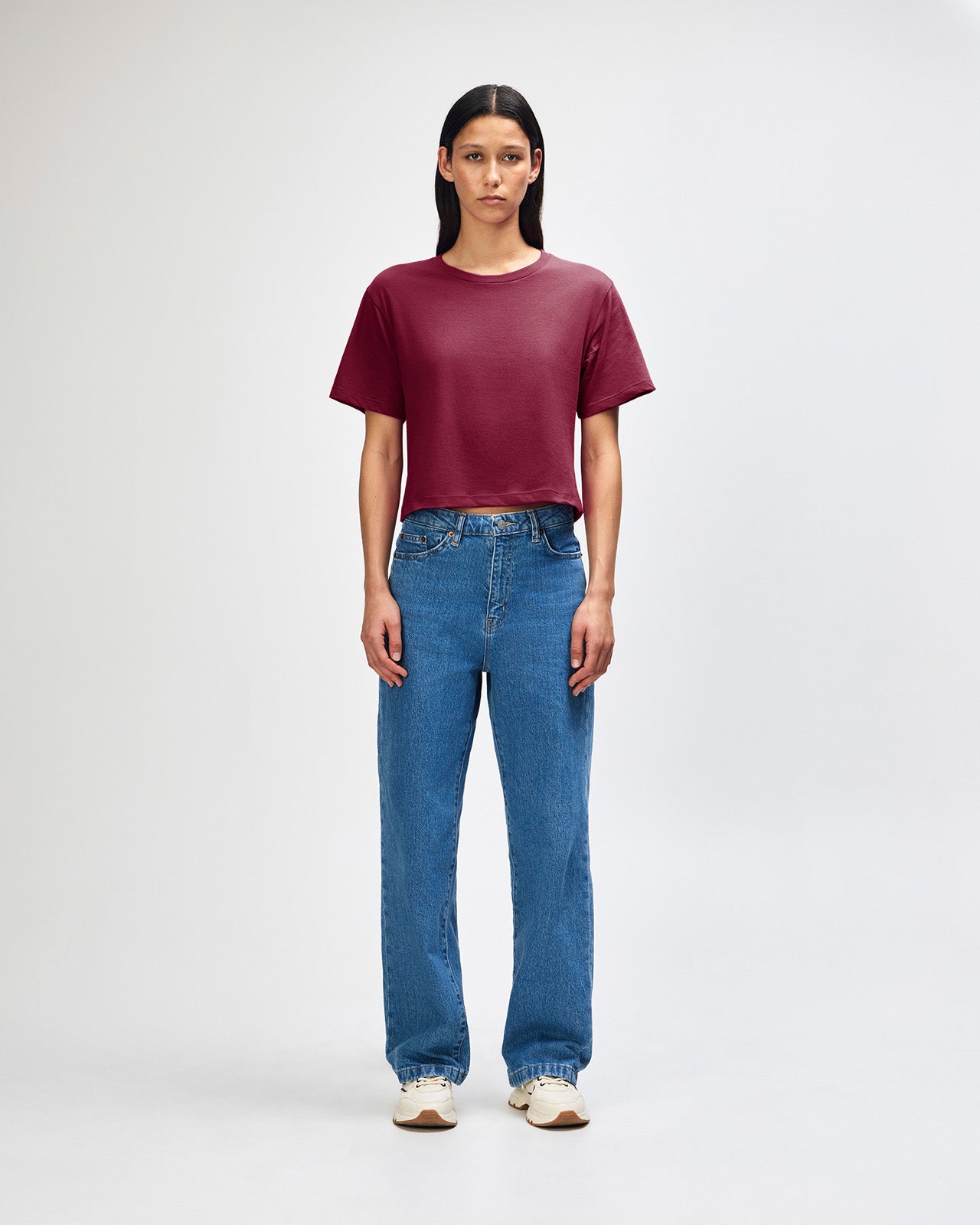 Female model wearing an American Apparel Fine Jersey Women's Boxy Tee in Burgundy, paired with blue jeans, standing against a plain background (front pose) -burgundy