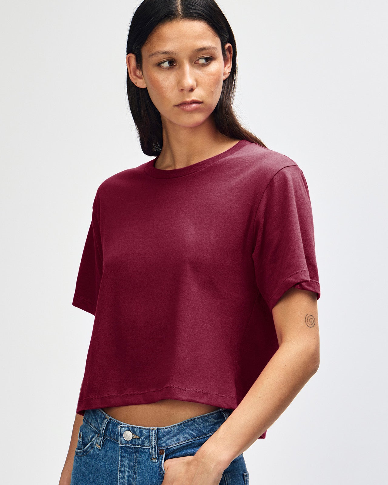Female model wearing an American Apparel Fine Jersey Women's Boxy Tee in Burgundy, paired with blue jeans, standing against a plain background (front pose) -burgundy