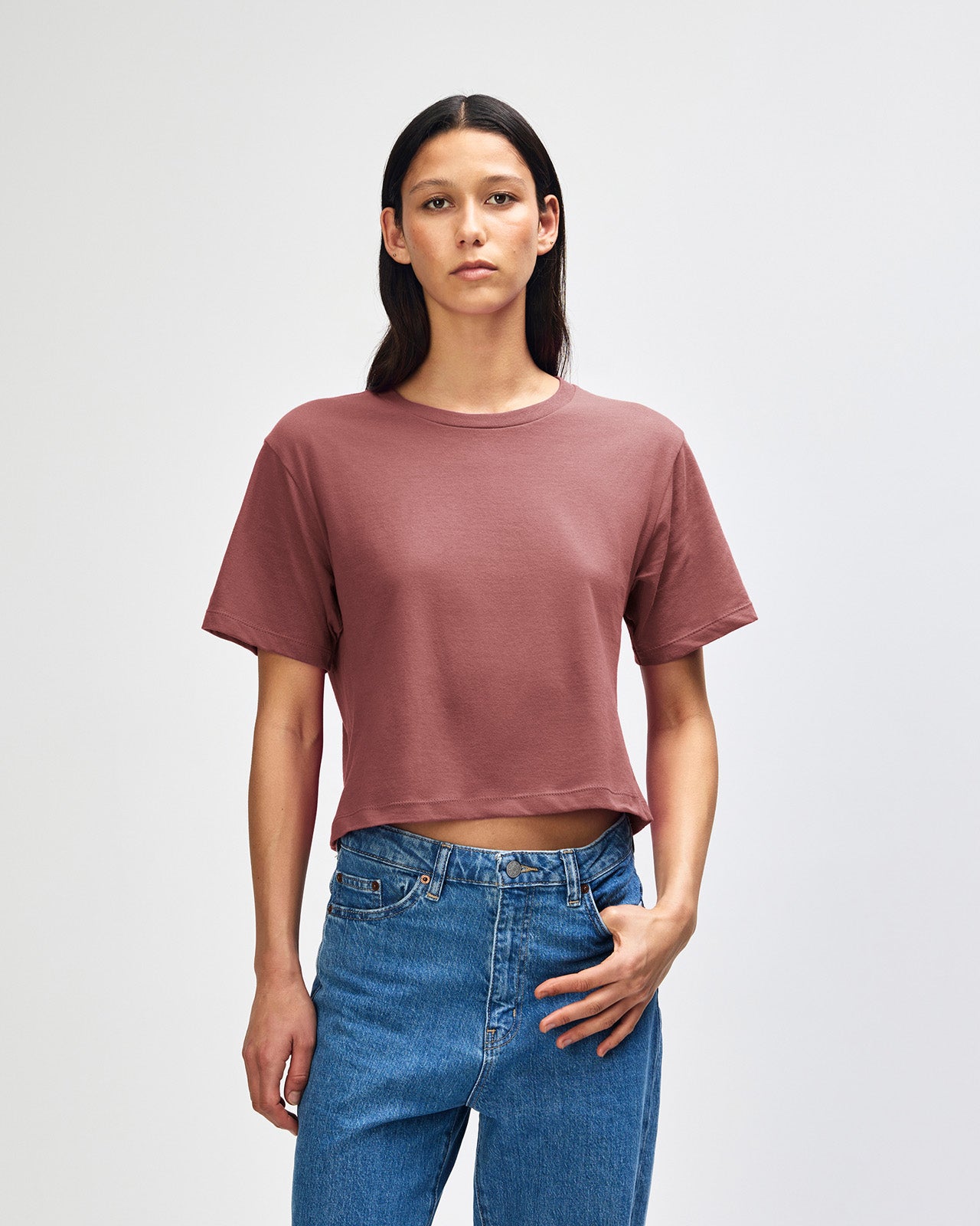 Female model wearing an American Apparel Fine Jersey Women's Boxy Tee in Burgundy, paired with blue jeans, standing against a plain background (front pose) -canyon