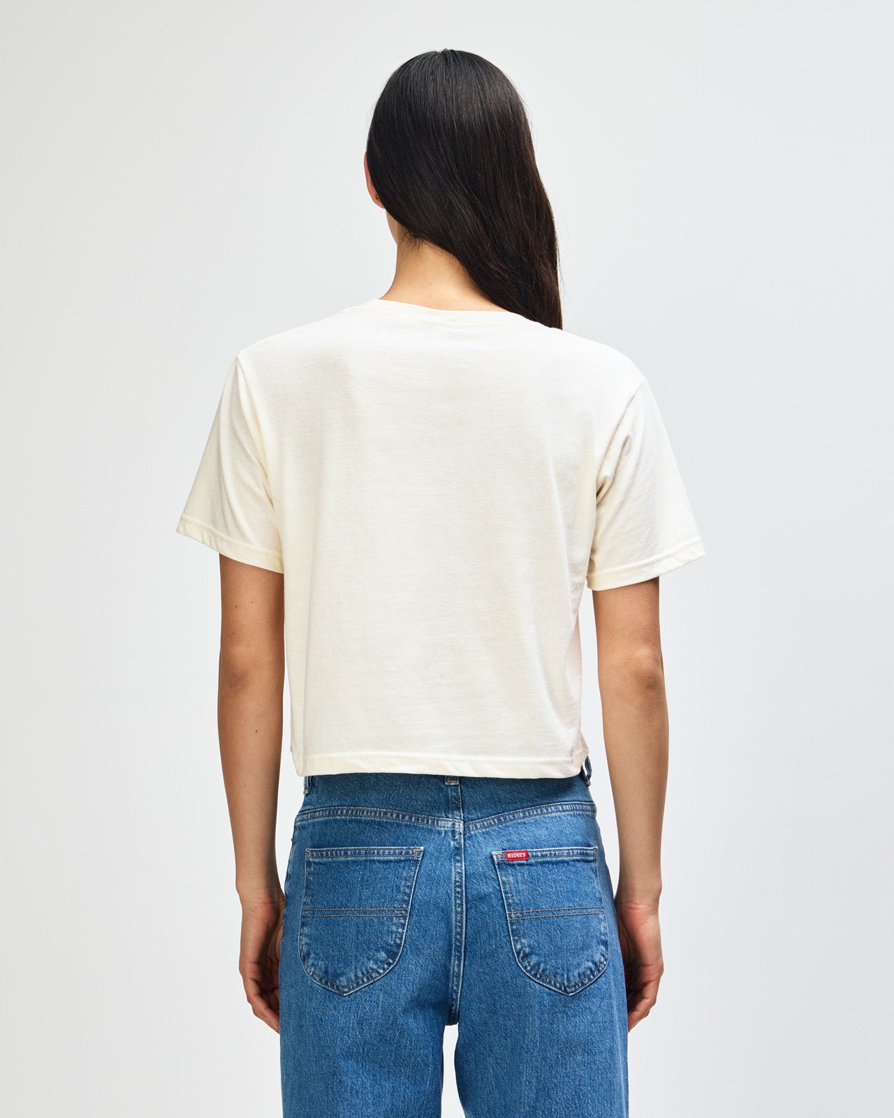 Female model wearing an American Apparel Fine Jersey Women's Boxy Tee in cream, paired with blue jeans, standing against a plain background (front pose) -cream