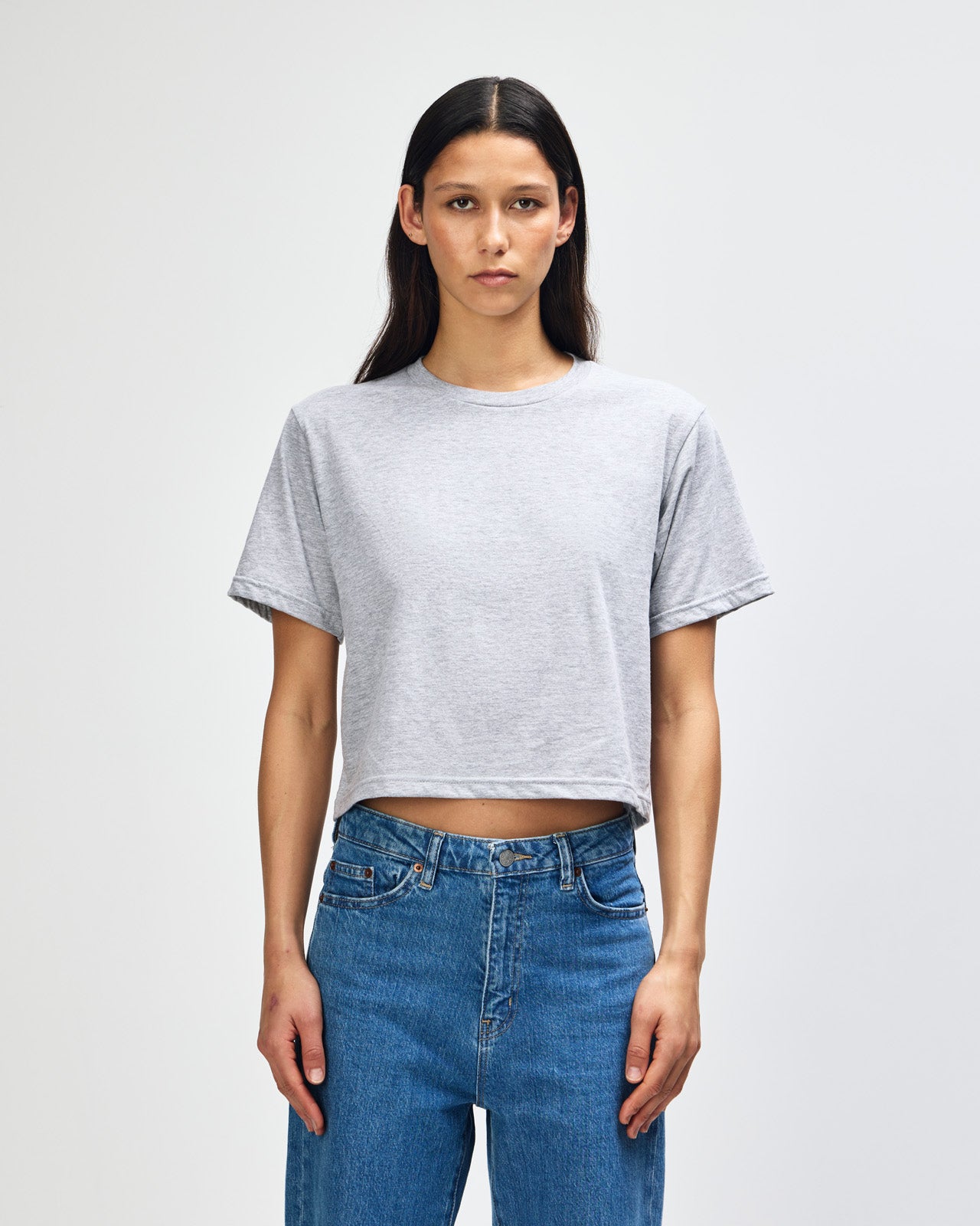 Female model wearing an American Apparel Fine Jersey Women's Boxy Tee in Heather Sport Grey, paired with black jeans, standing against a plain background (front pose) -heather grey