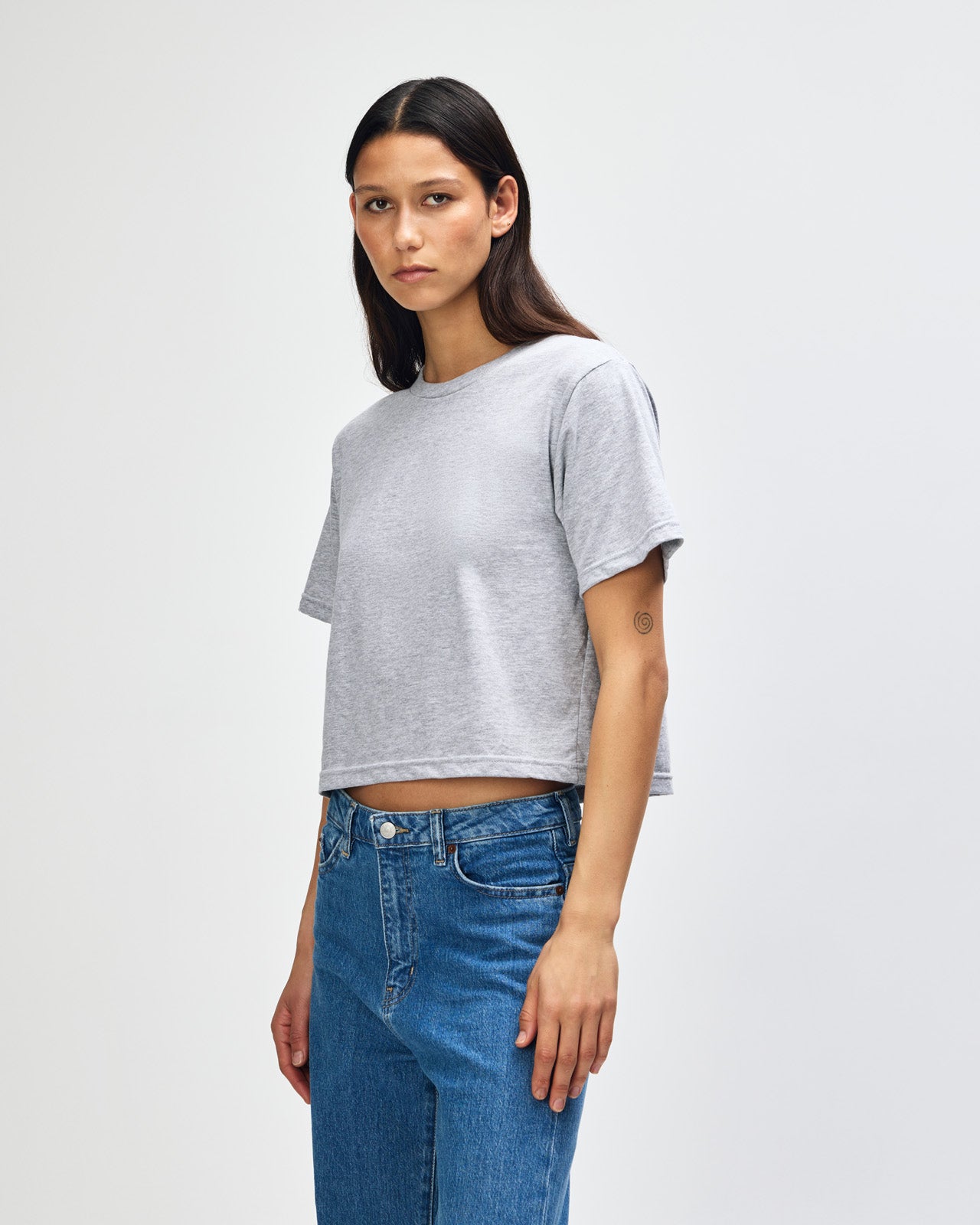 Female model wearing an American Apparel Fine Jersey Women's Boxy Tee in Heather Sport Grey, paired with black jeans, standing against a plain background (front pose) -heather grey