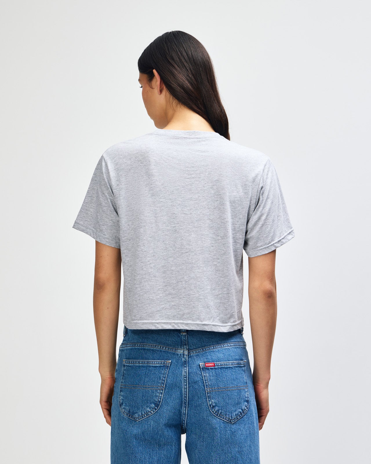 Female model wearing an American Apparel Fine Jersey Women's Boxy Tee in Heather Sport Grey, paired with black jeans, standing against a plain background (front pose) -heather grey