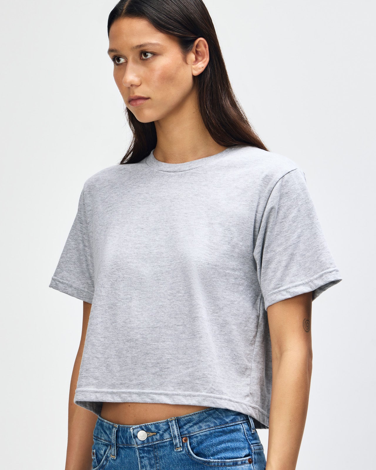 Female model wearing an American Apparel Fine Jersey Women's Boxy Tee in Heather Sport Grey, paired with black jeans, standing against a plain background (front pose) -heather grey