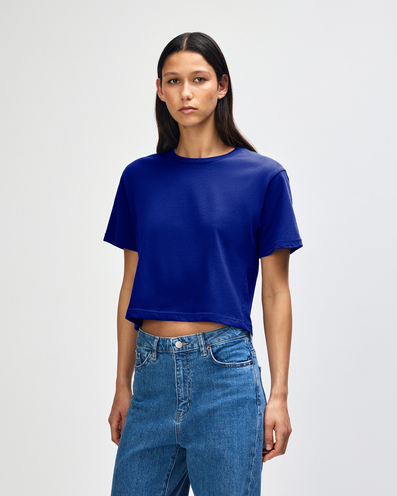 Female model wearing an American Apparel Fine Jersey Women's Boxy Tee in Lapis, paired with blue jeans, standing against a plain background (front pose) -lapis