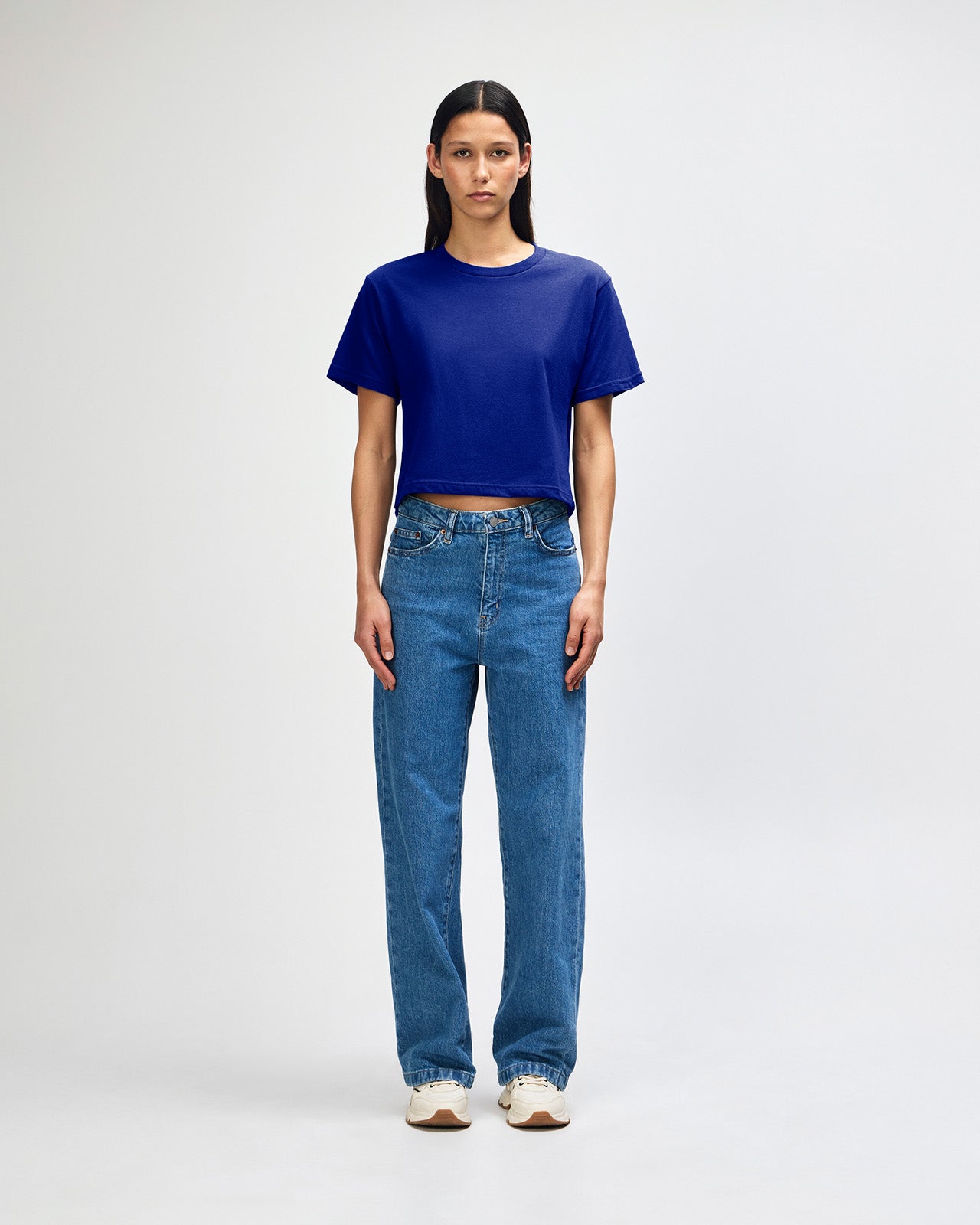 Female model wearing an American Apparel Fine Jersey Women's Boxy Tee in Lapis, paired with blue jeans, standing against a plain background (front pose) -lapis