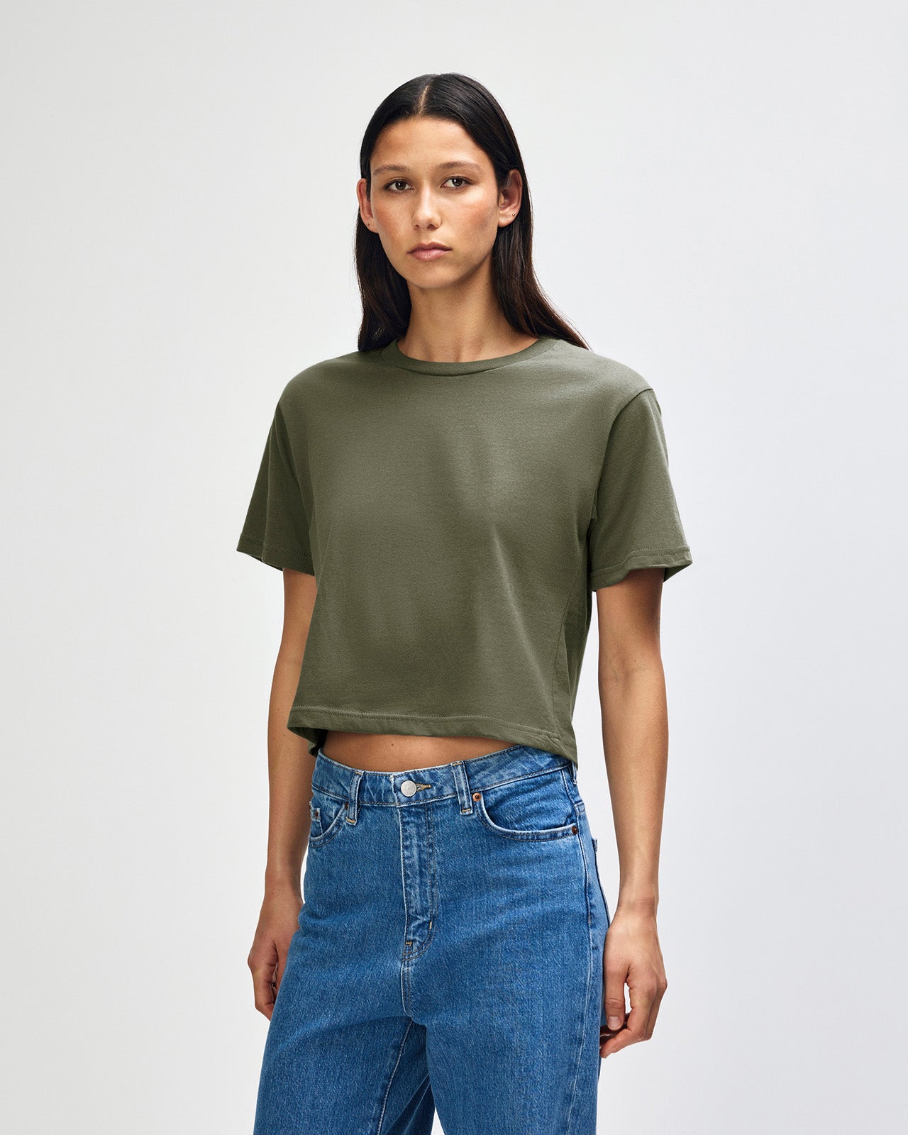 Female model wearing an American Apparel Fine Jersey Women's Boxy Tee in Lieutenant, paired with blue jeans, standing against a plain background (front pose) -lieutenant