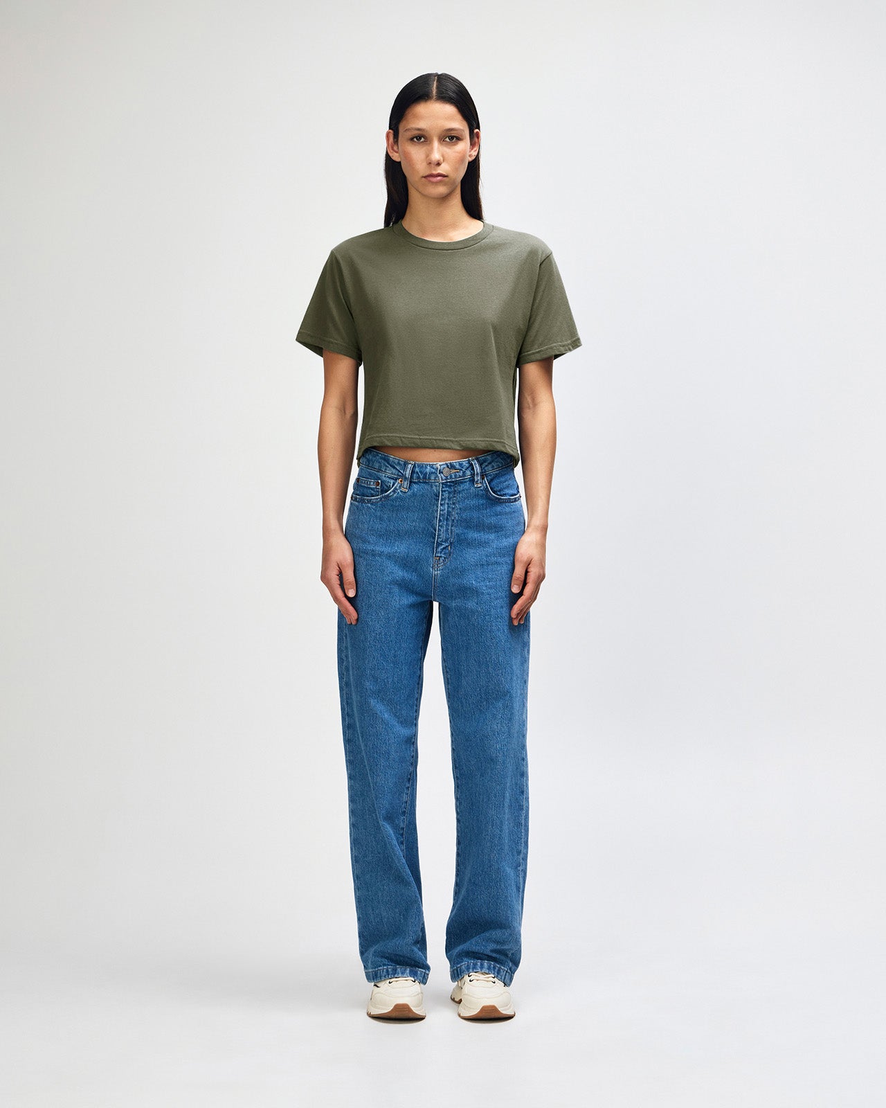 Female model wearing an American Apparel Fine Jersey Women's Boxy Tee in Lieutenant, paired with blue jeans, standing against a plain background (front pose) -lieutenant