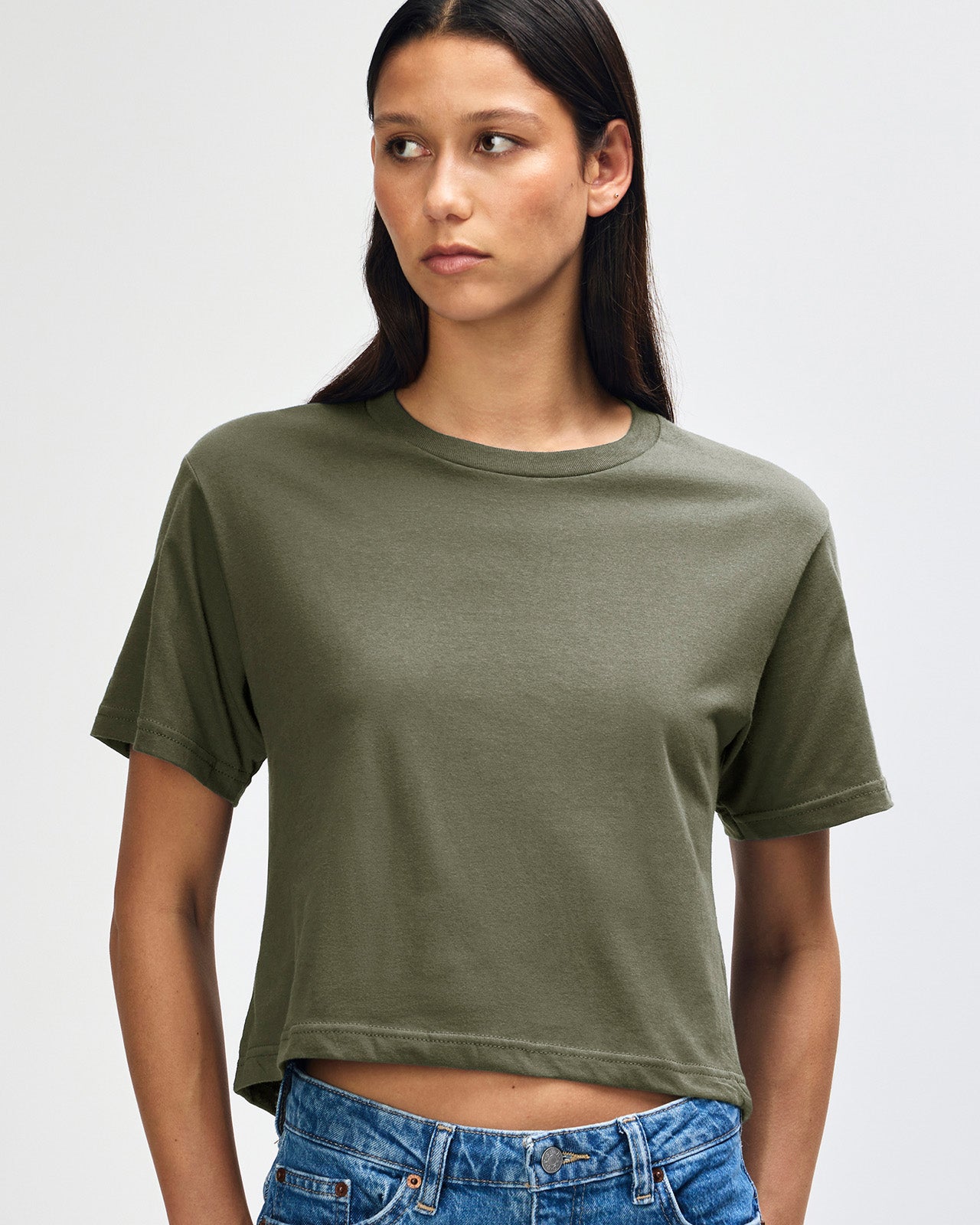 Female model wearing an American Apparel Fine Jersey Women's Boxy Tee in Lieutenant, paired with blue jeans, standing against a plain background (front pose) -lieutenant