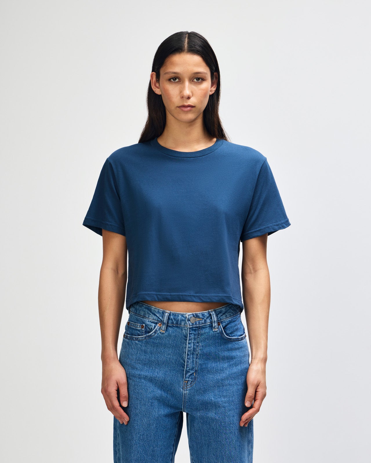 Female model wearing an American Apparel Fine Jersey Women's Boxy Tee in Sea Blue, paired with blue jeans, standing against a plain background (front pose) -sea blue